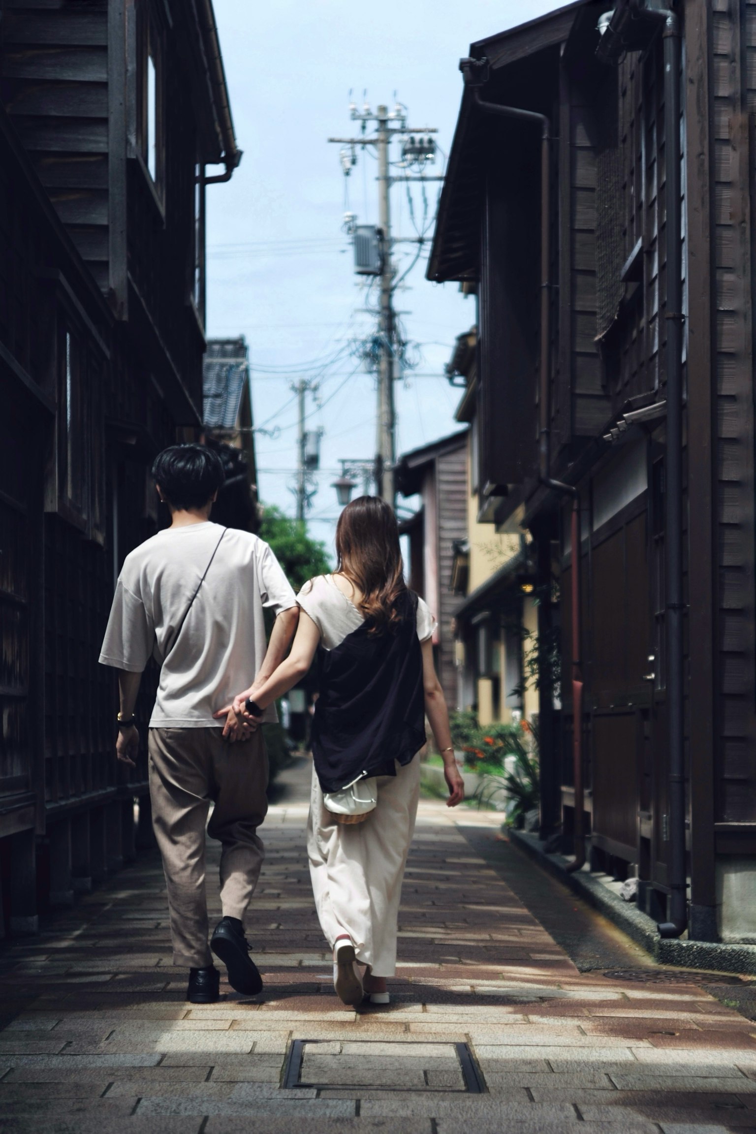 คู่รักเดินจับมือกันในซอยแคบที่มีอาคารไม้แบบดั้งเดิม