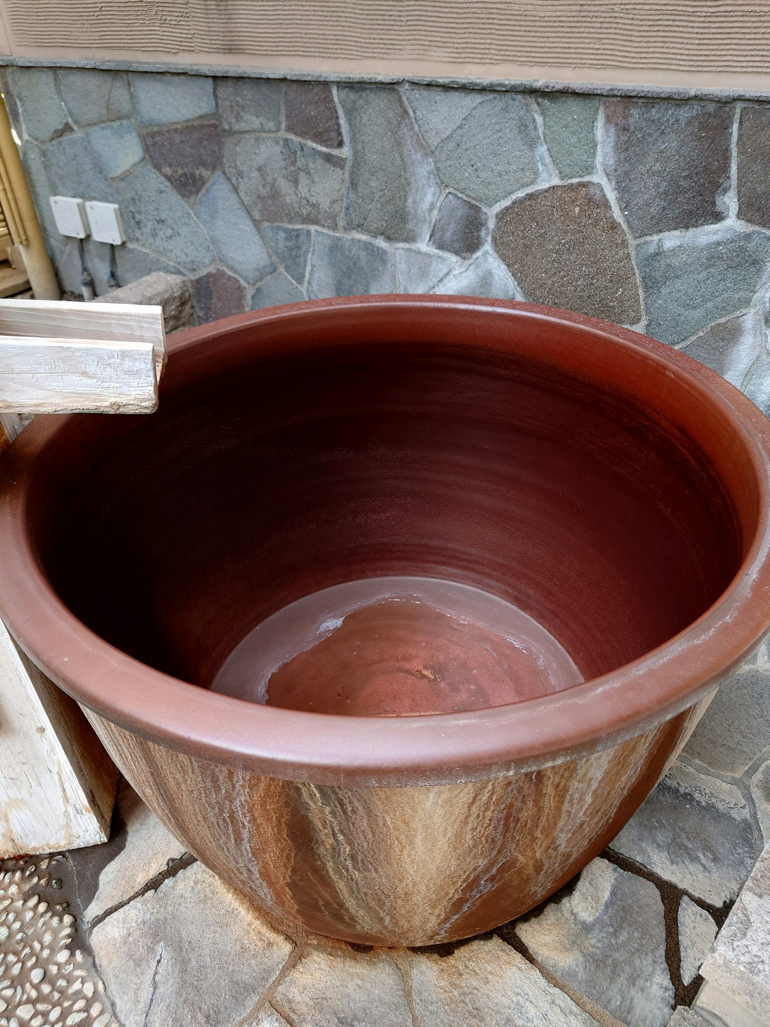 Brown ceramic pot positioned in front of a stone wall