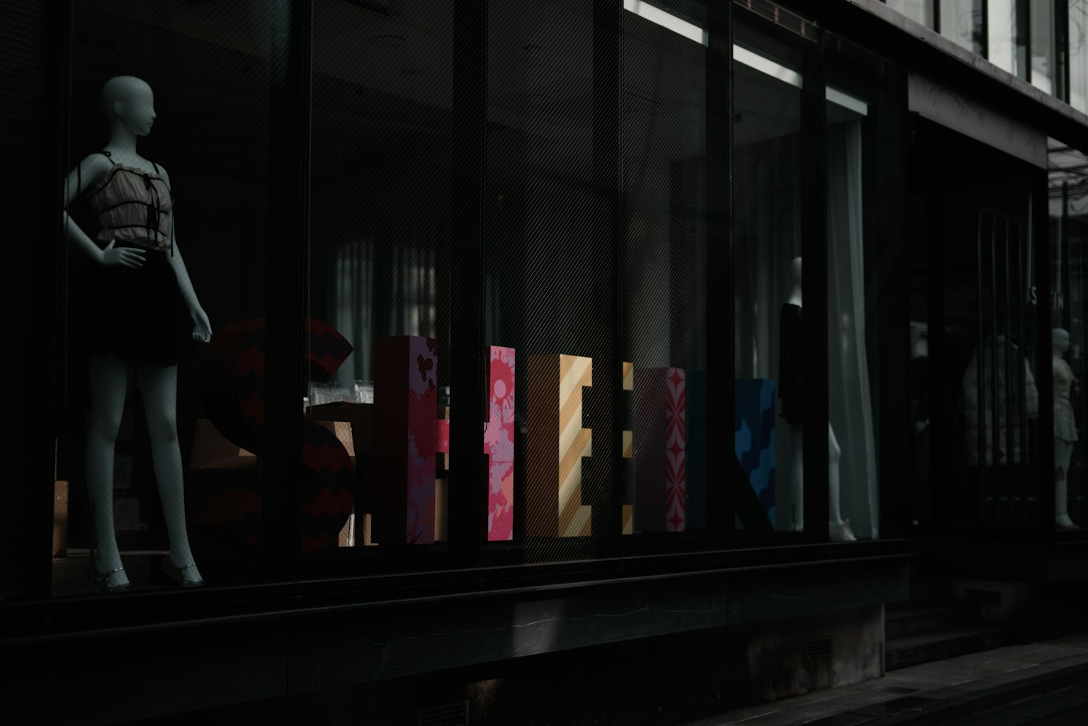 Mannequin in a shop window with colorful letters in a dark street