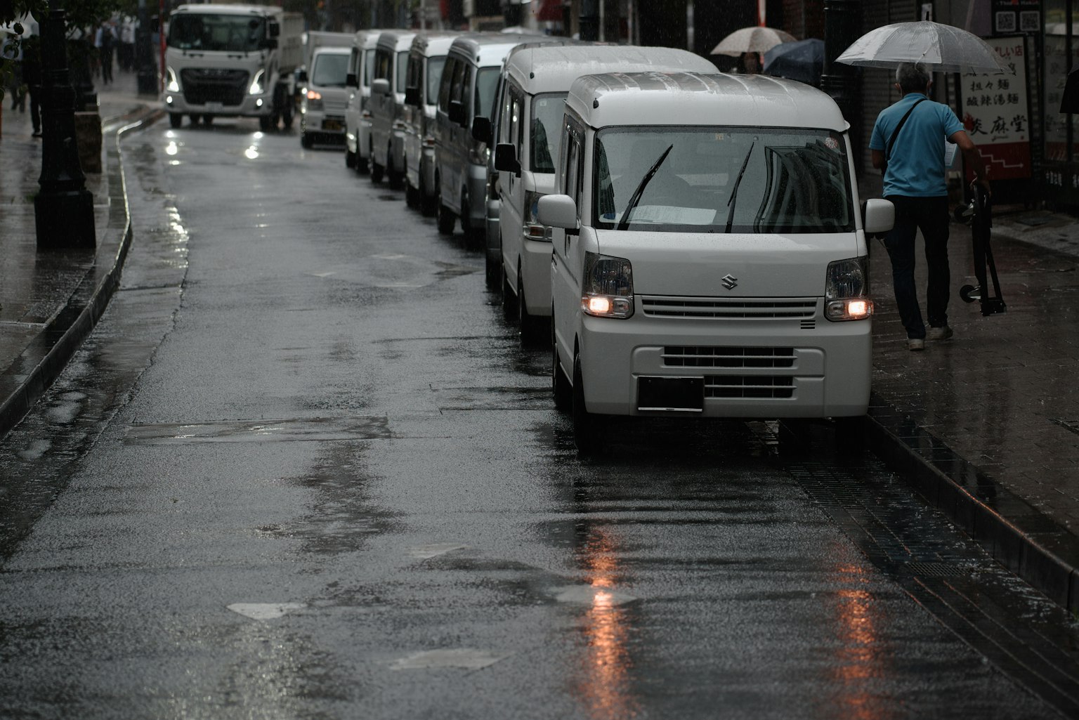 Rangée de petits camions blancs sur une rue pluvieuse avec une personne tenant un parapluie