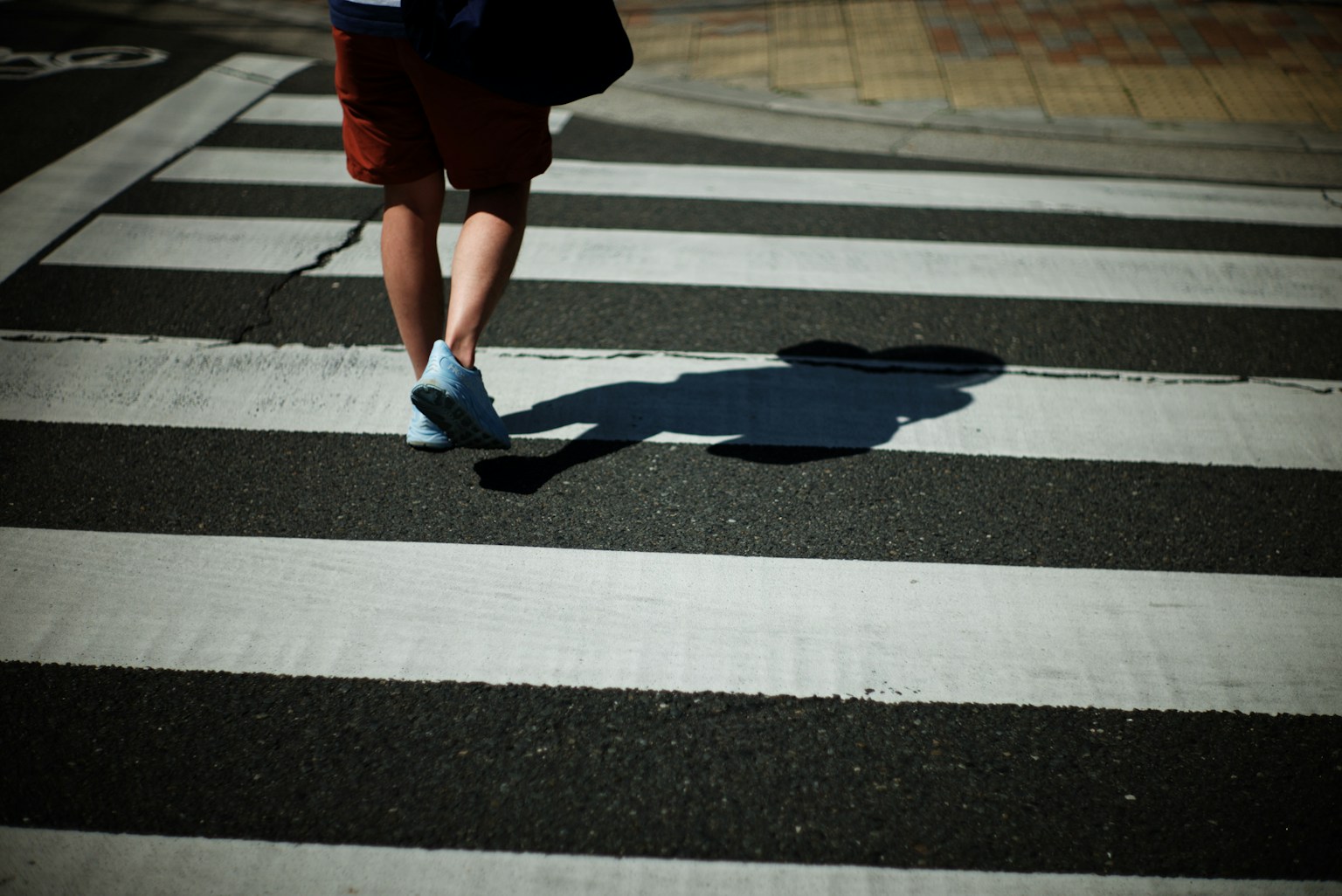 A person walking on a crosswalk with visible legs and shadow