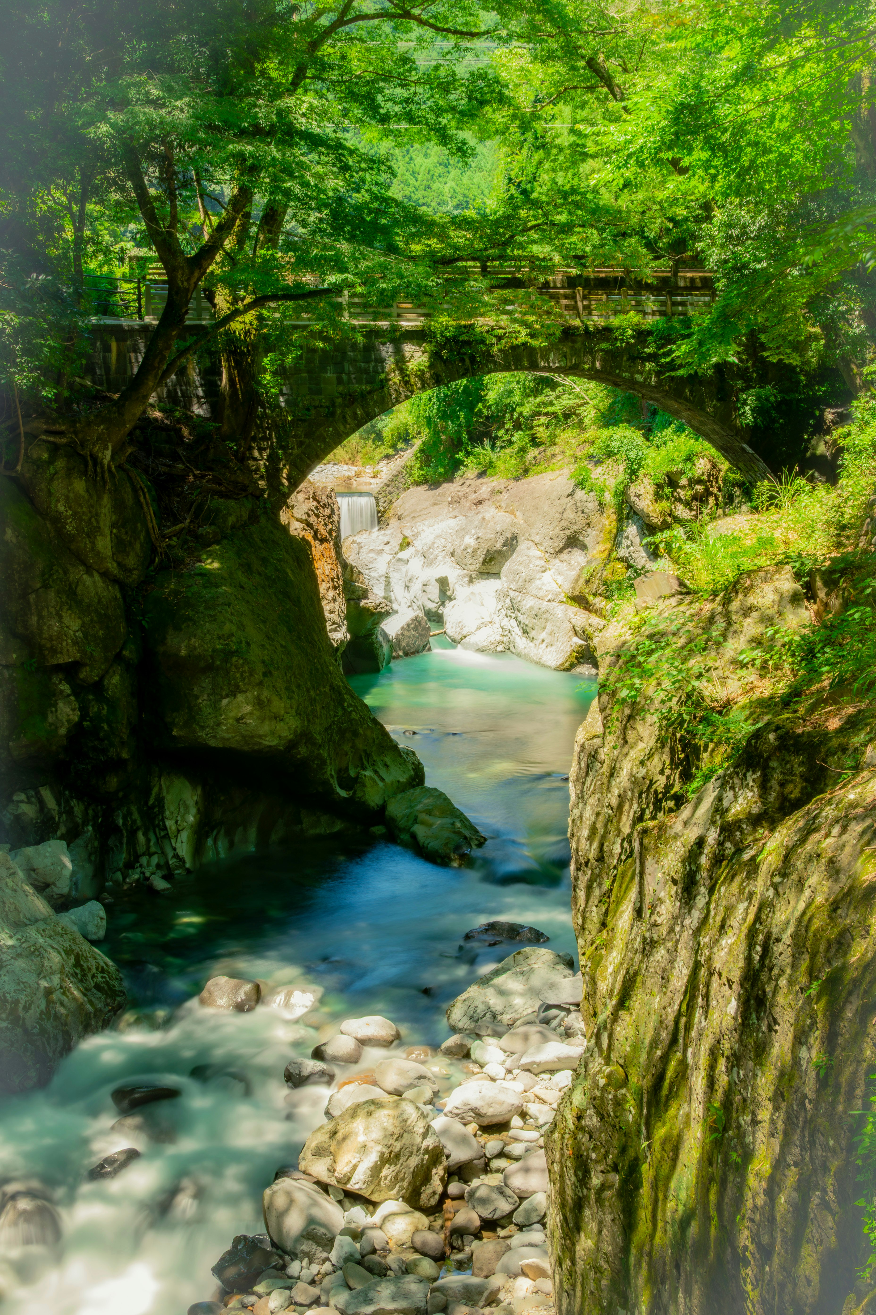 緑の木々に囲まれた渓流と石積みの小さな橋のある風景