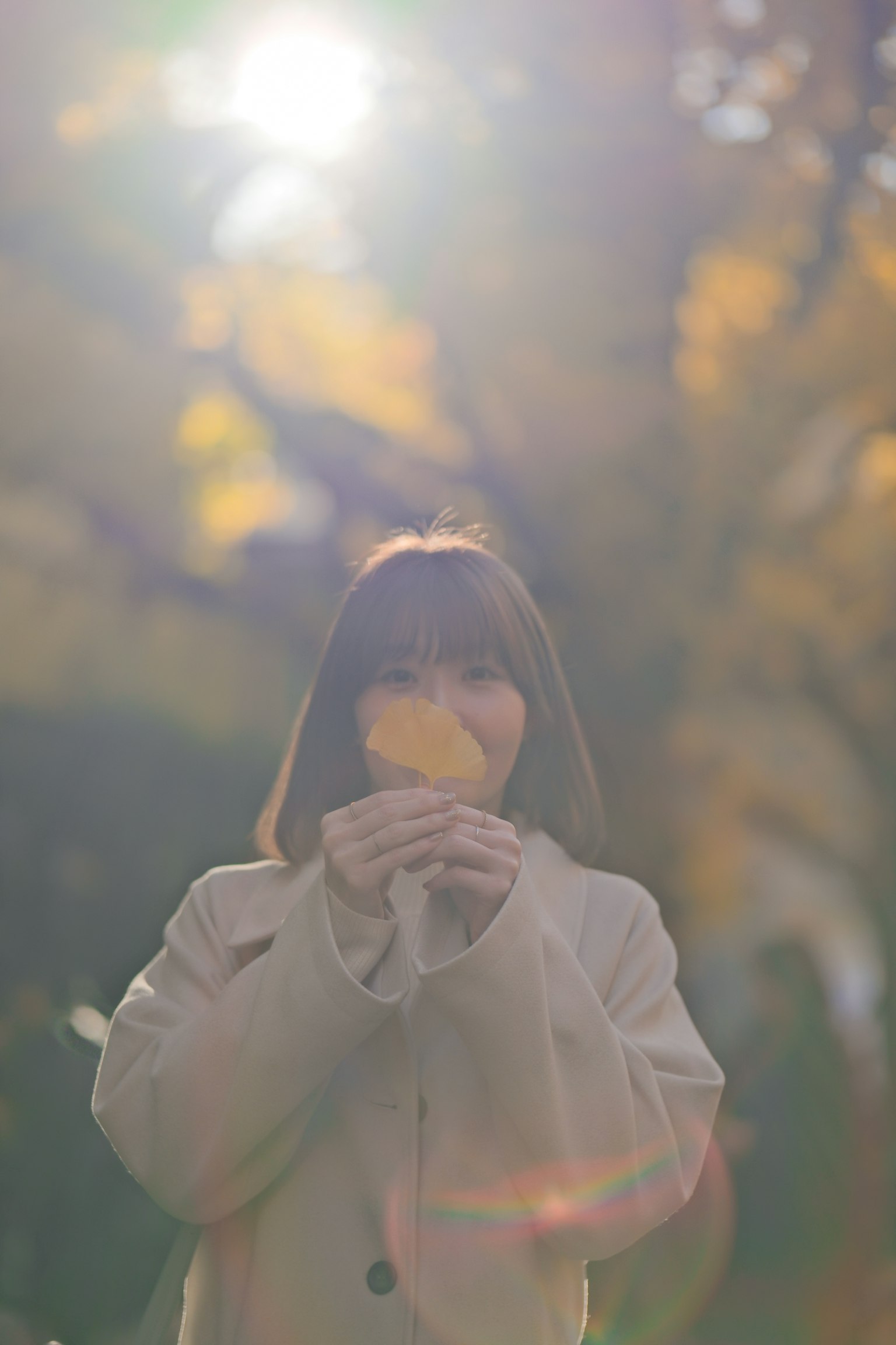 一位女士在秋天的公园里手持一片叶子，阳光从她身后照射