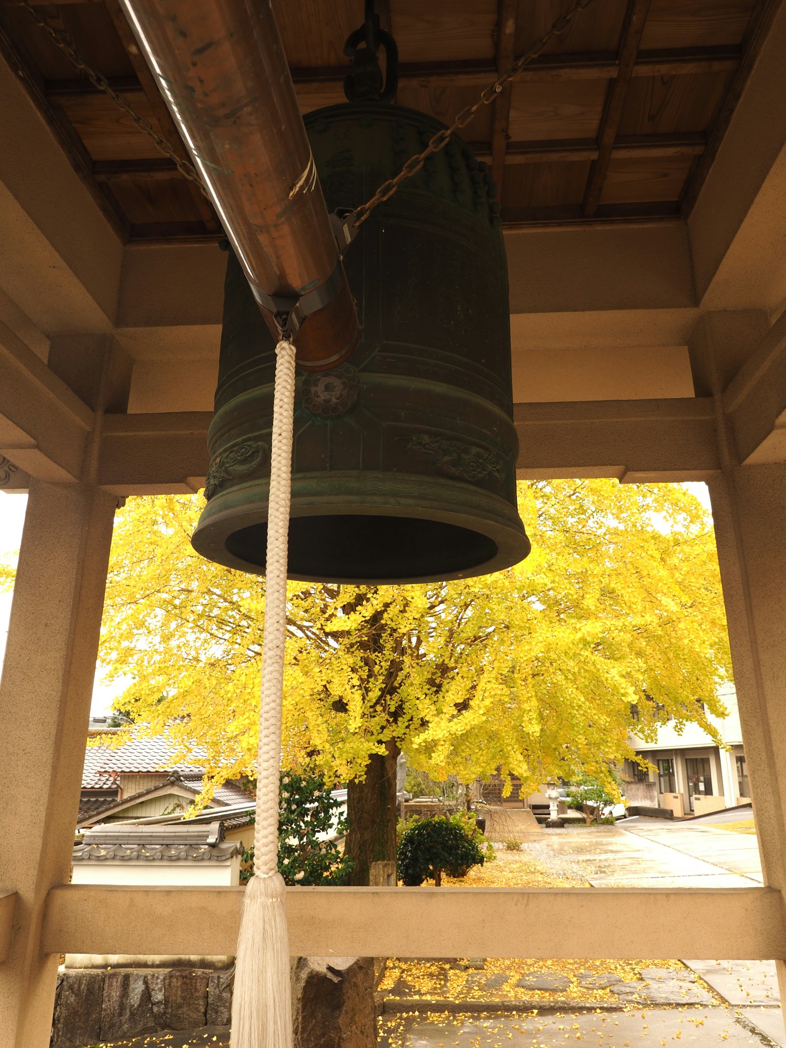 ระฆังทองเหลืองขนาดใหญ่ภายในหอระฆังที่มีใบไม้สีเหลืองอยู่ด้านหลัง
