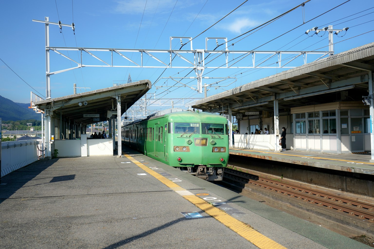 Treno verde in una stazione con banchine e cielo blu