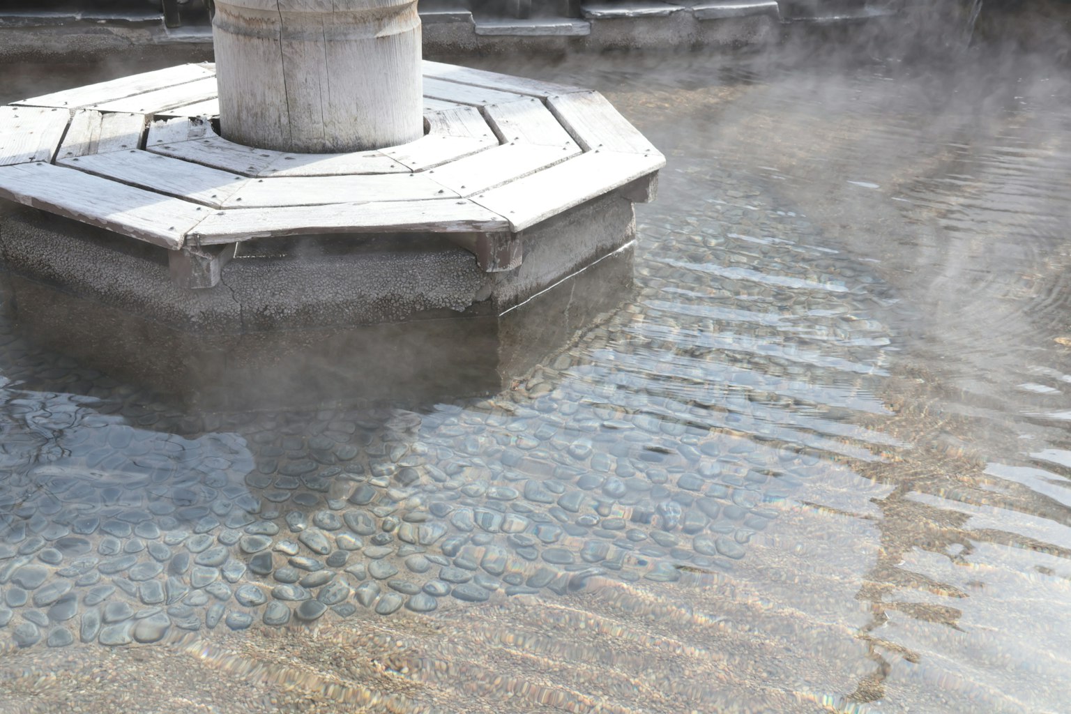 Struttura ottagonale con base in pietra e vapore che sale dall'acqua termale