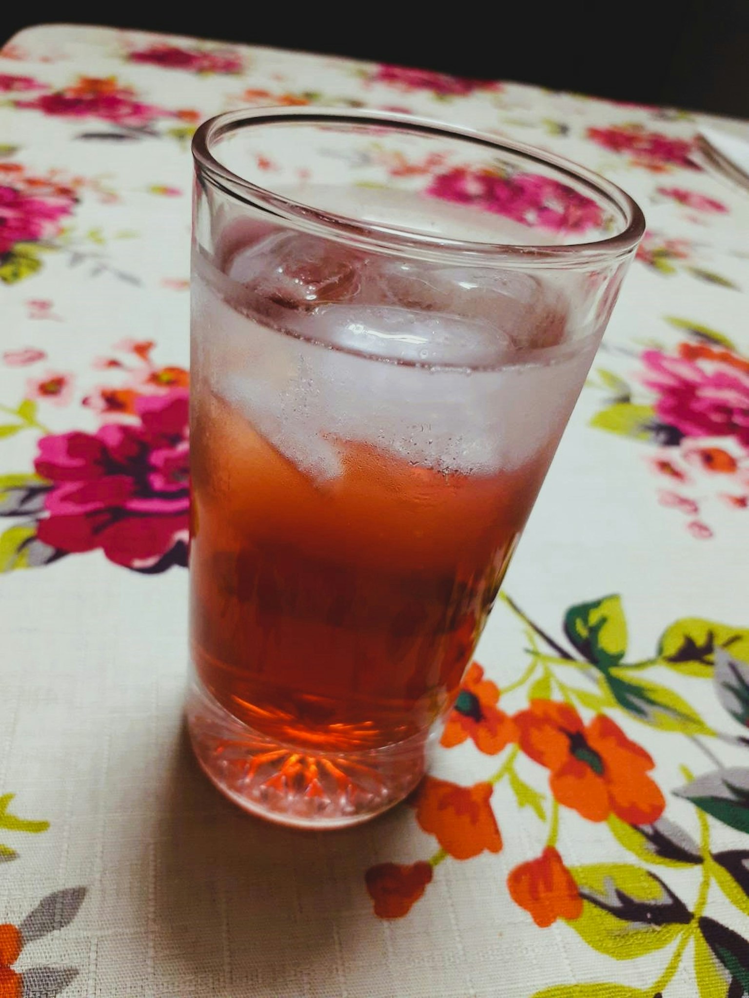Un verre de boisson rouge avec de la glace sur une nappe florale