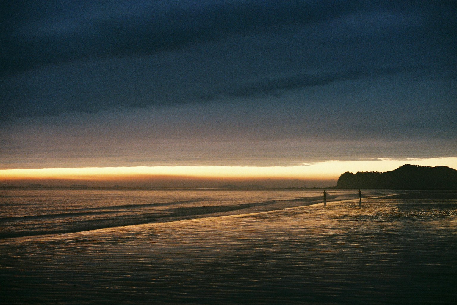 夕暮れ時の海岸線に人々が歩いている風景