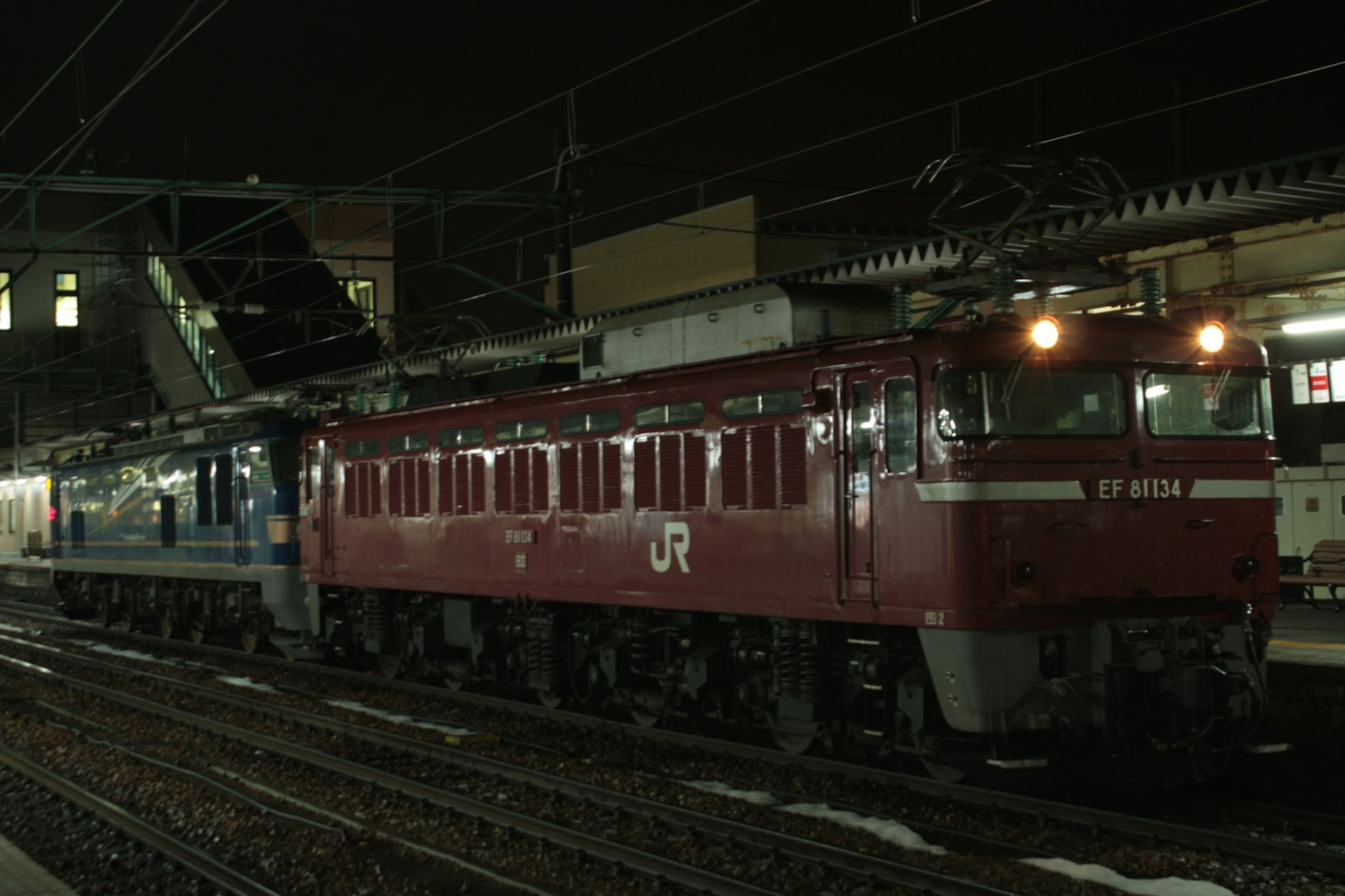 Locomotive électrique rouge et train bleu arrêtés à la gare de nuit