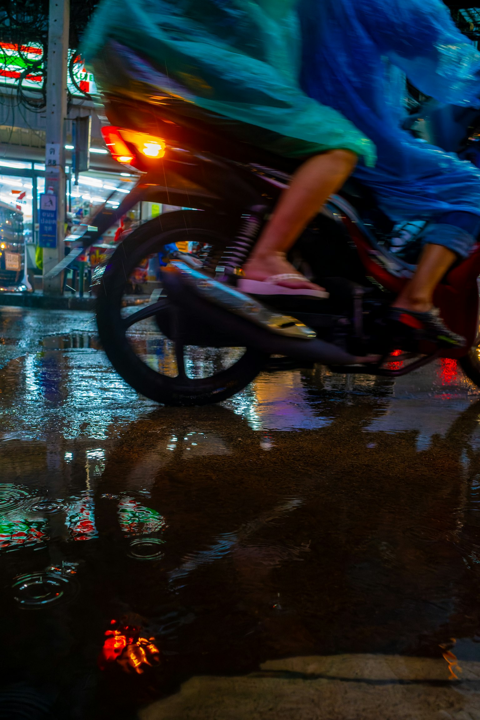 Seseorang mengendarai sepeda motor di bawah hujan dengan pantulan di genangan air di jalan