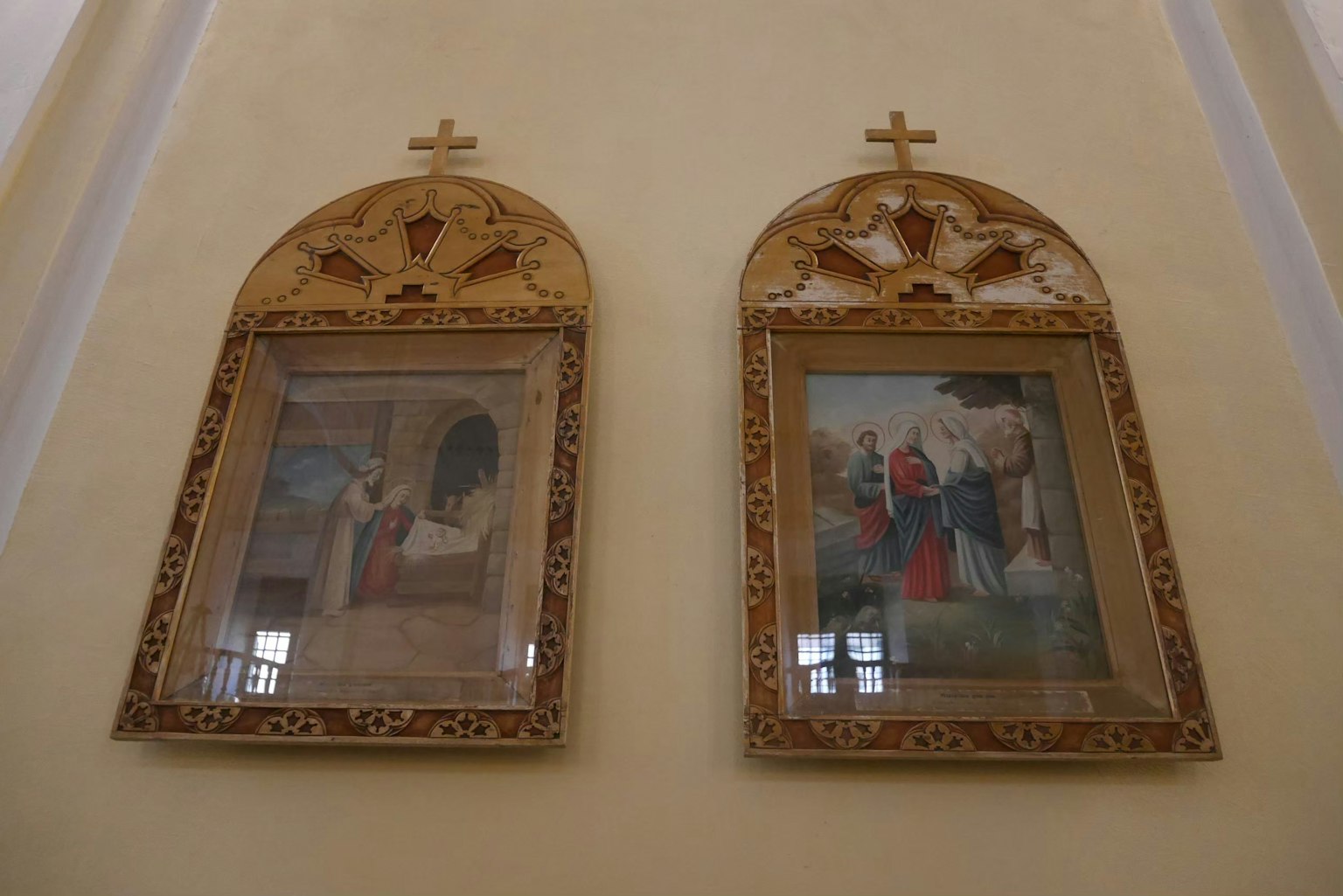 Due dipinti religiosi incorniciati in decorazioni ornate appesi a un muro di chiesa