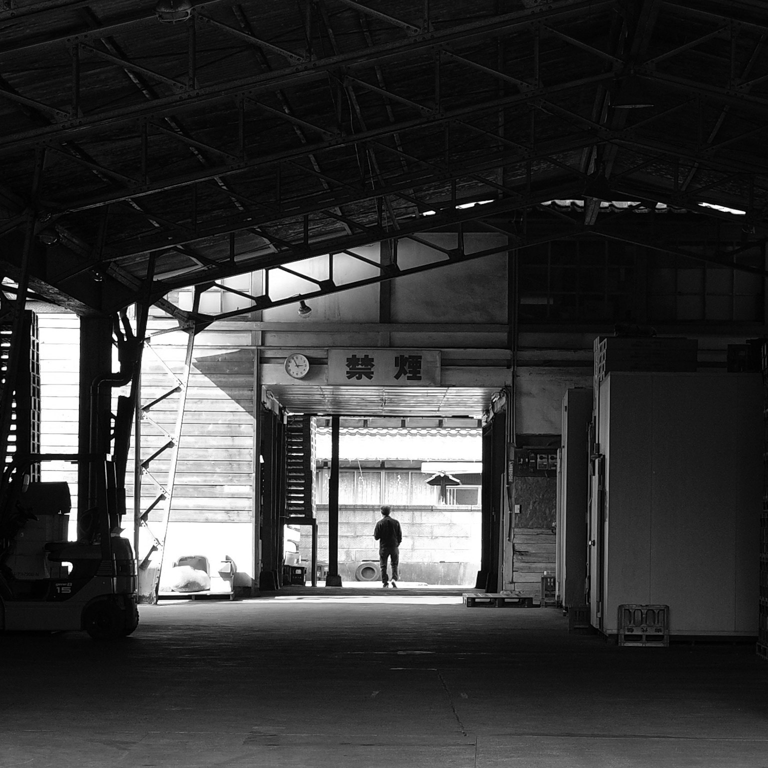 Une personne se tenant à l'intérieur d'un espace industriel en noir et blanc marchant vers l'entrée