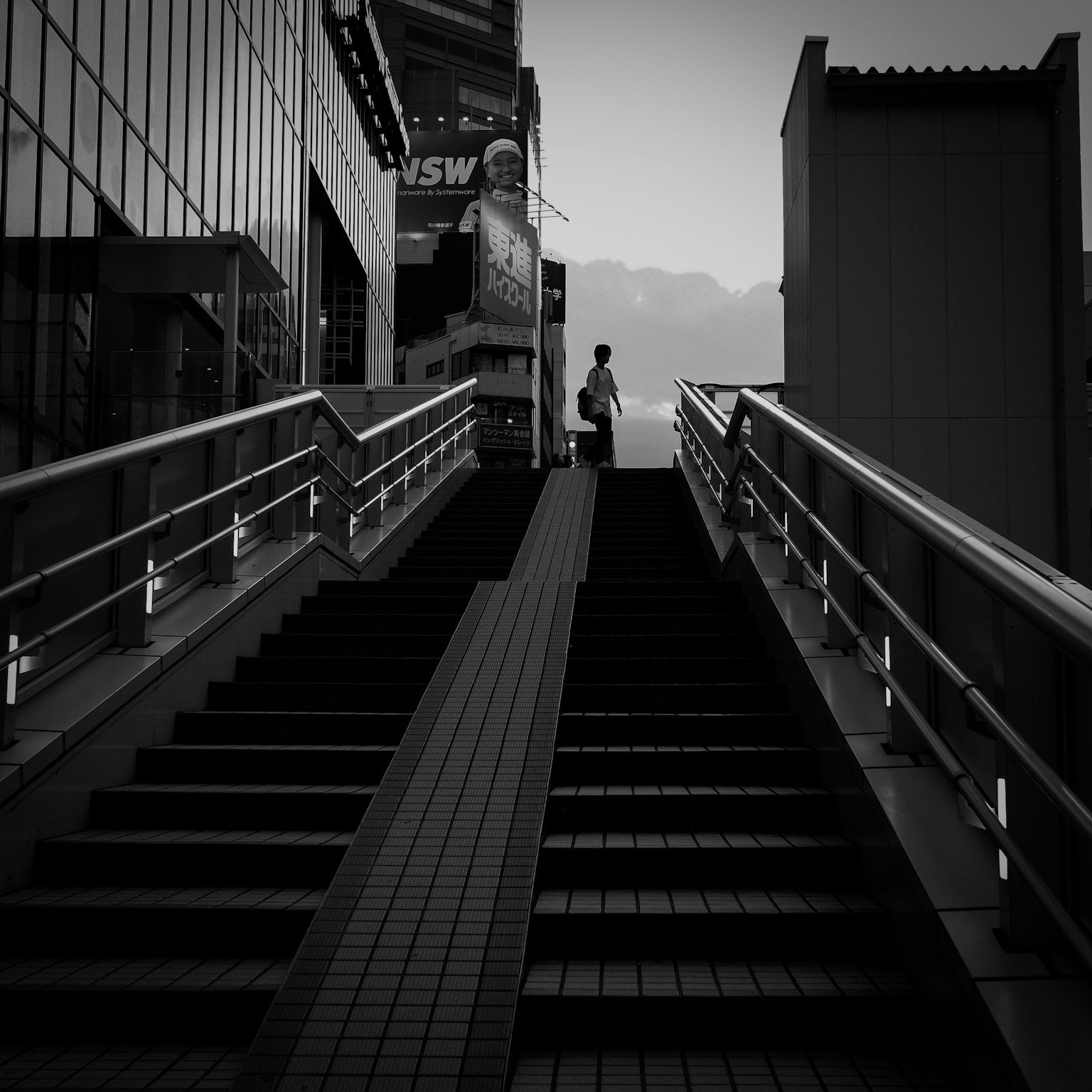 階段を上る人のシルエットとモノクロの都市風景