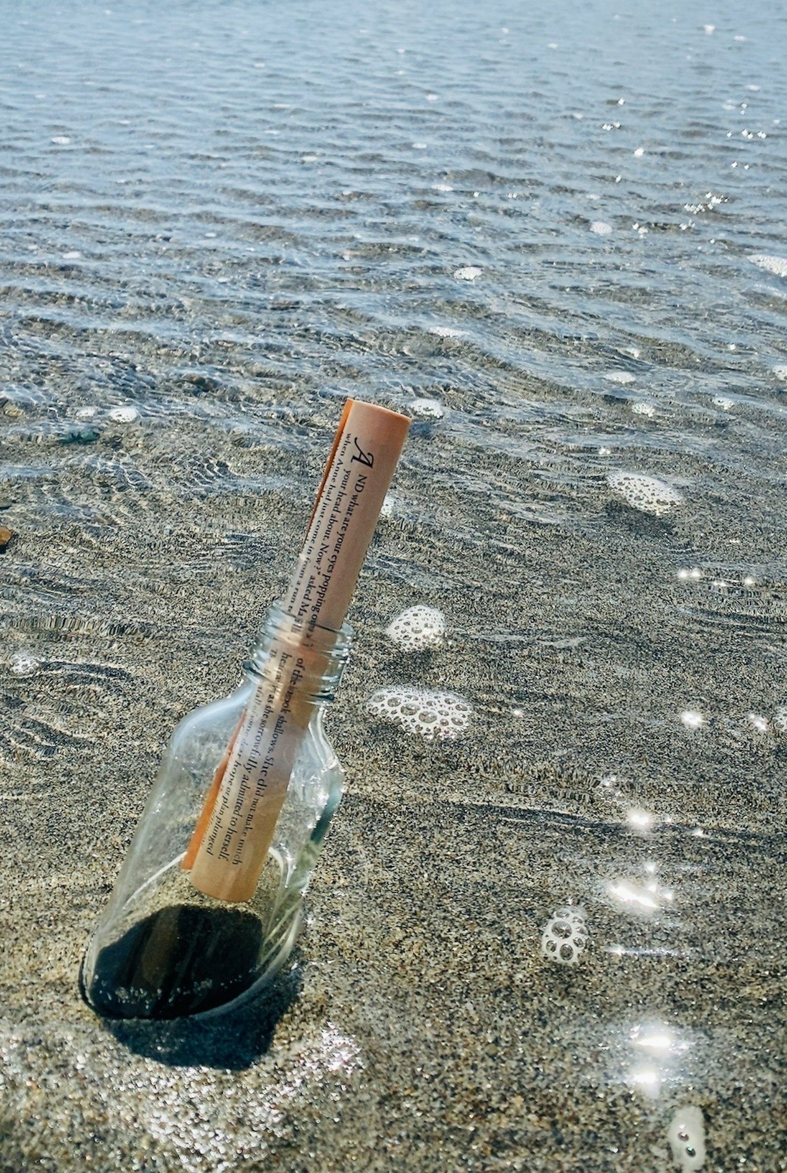 Una bottiglia con un messaggio appoggiata su una spiaggia sabbiosa con onde leggere