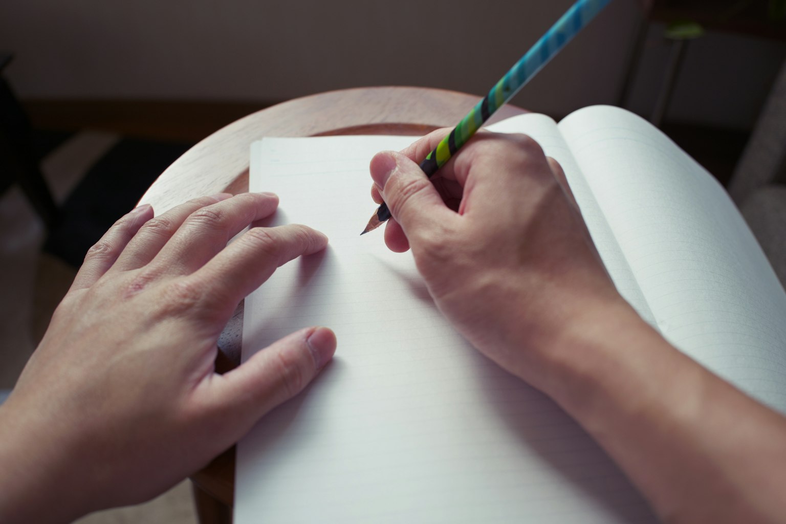 Hände, die mit einem Bleistift in ein leeres Notizbuch schreiben
