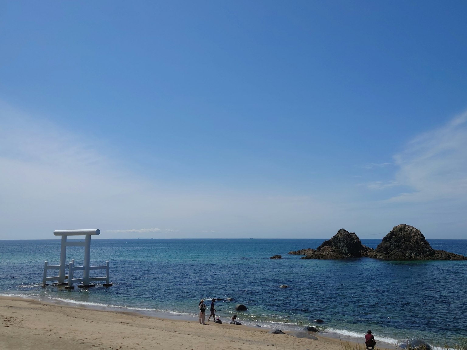 Puerta torii en la playa con formaciones rocosas y cielo azul claro