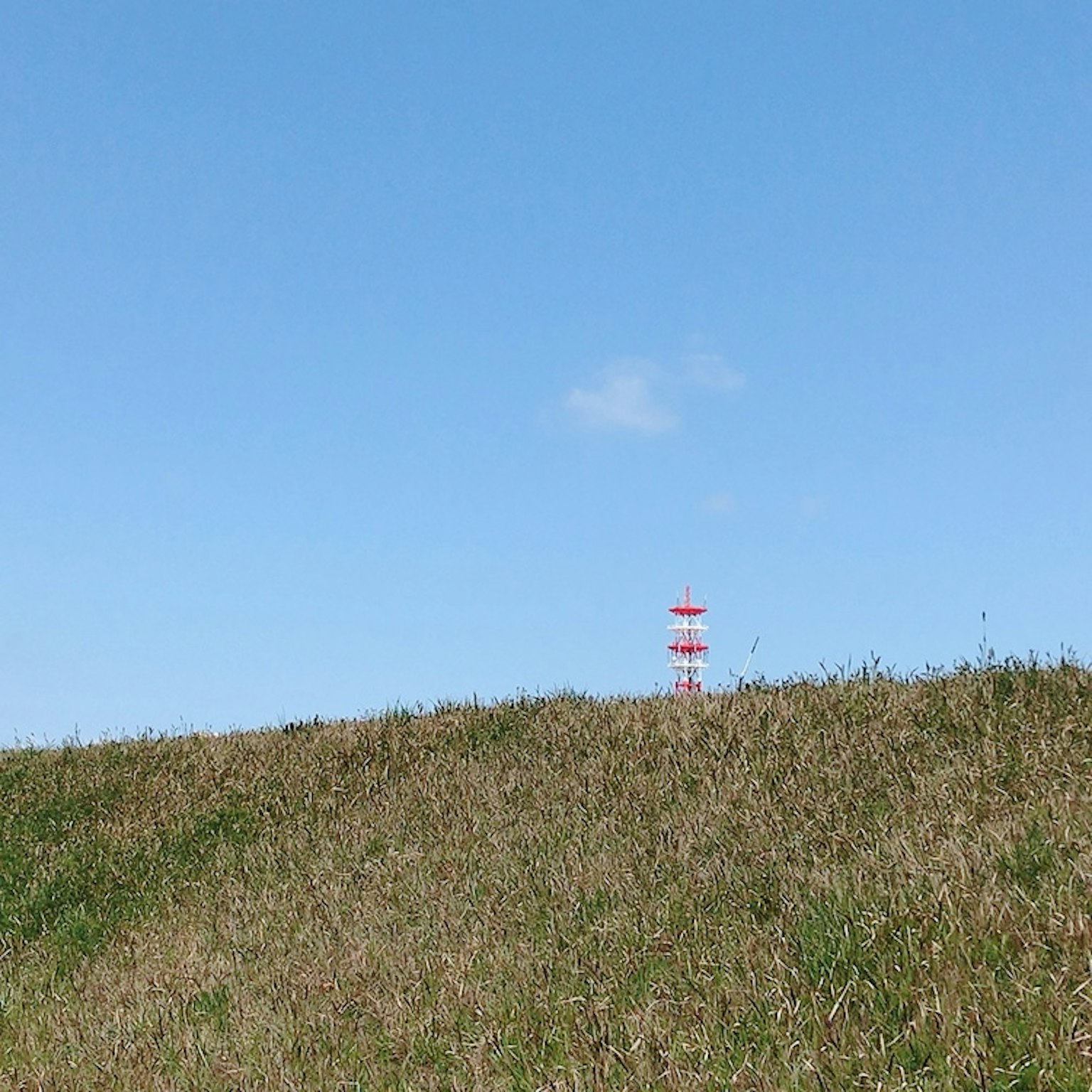 Ein rot-weißer Turm steht auf einem grünen Hügel unter einem blauen Himmel