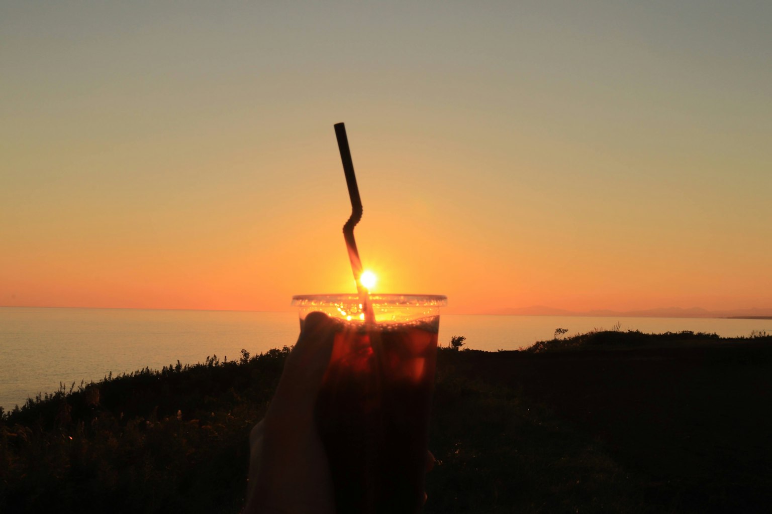Un verre de boisson avec une paille en silhouette contre le coucher de soleil