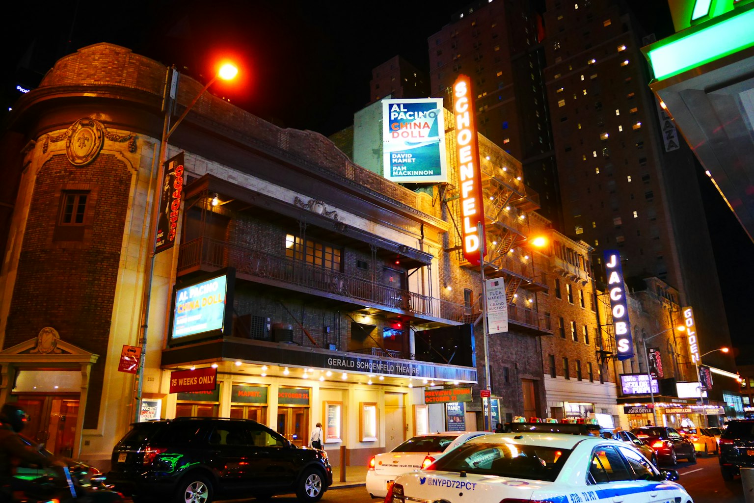 Exterior de un teatro por la noche con letreros de neón brillantes y coches aparcados