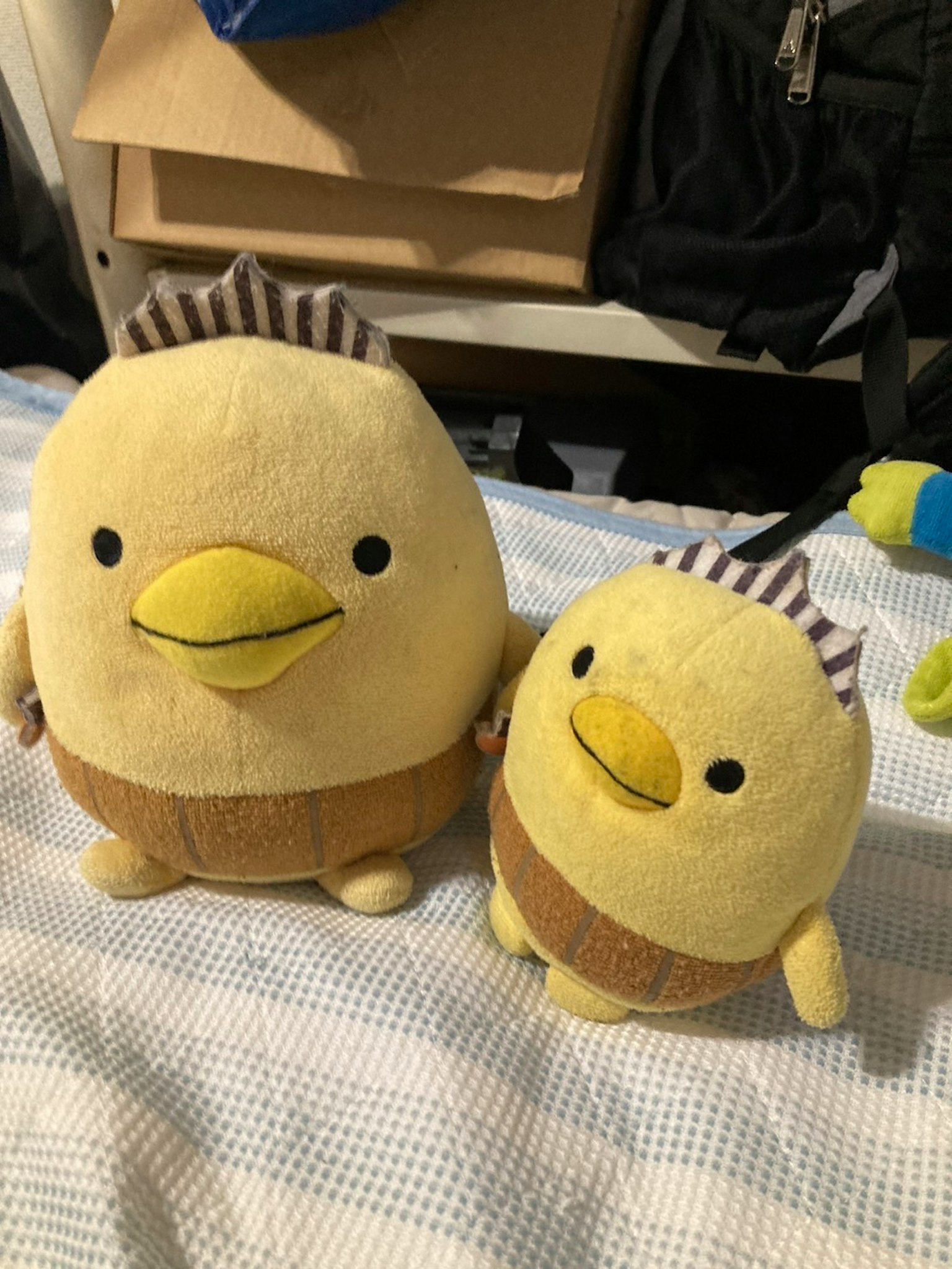 Due giocattoli di peluche a forma di uccello sono affiancati Il peluche più grande è giallo con dettagli marroni Il peluche più piccolo ha lo stesso design ma è più piccolo