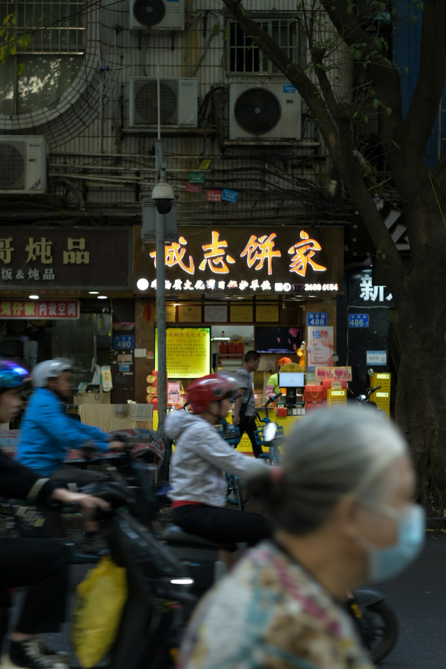 夜の街並みでバイクに乗る人々と飲食店の看板が見える
