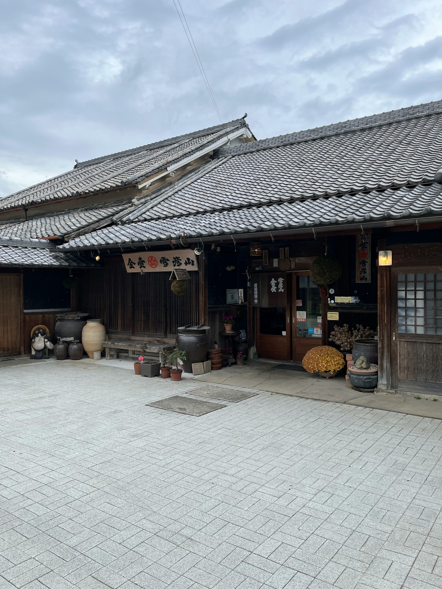 Vista exterior de una casa japonesa tradicional con un camino de piedra y barriles de madera
