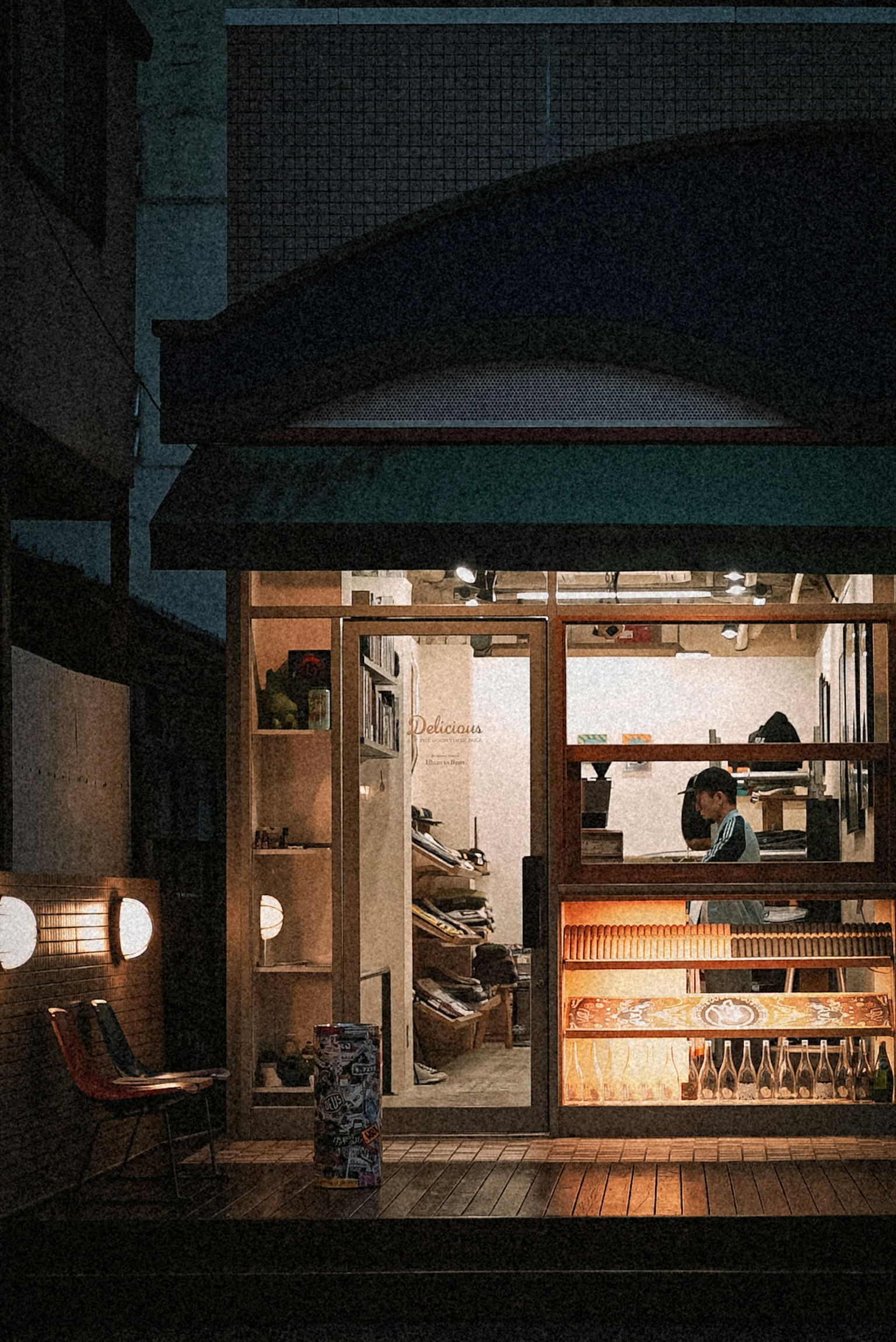 Exterior de una pequeña tienda con iluminación cálida en una calle oscura con estanterías de madera y productos exhibidos dentro