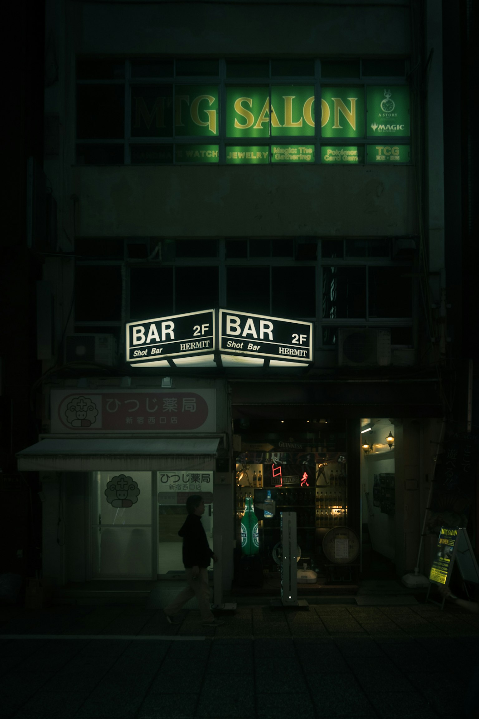Entrée d'un bar avec des enseignes au néon et un salon au-dessus la nuit