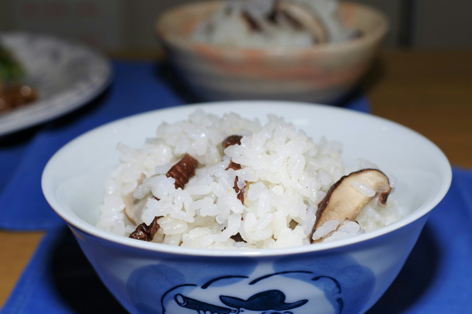 Semangkuk nasi putih dengan jamur shiitake di atas alas meja biru