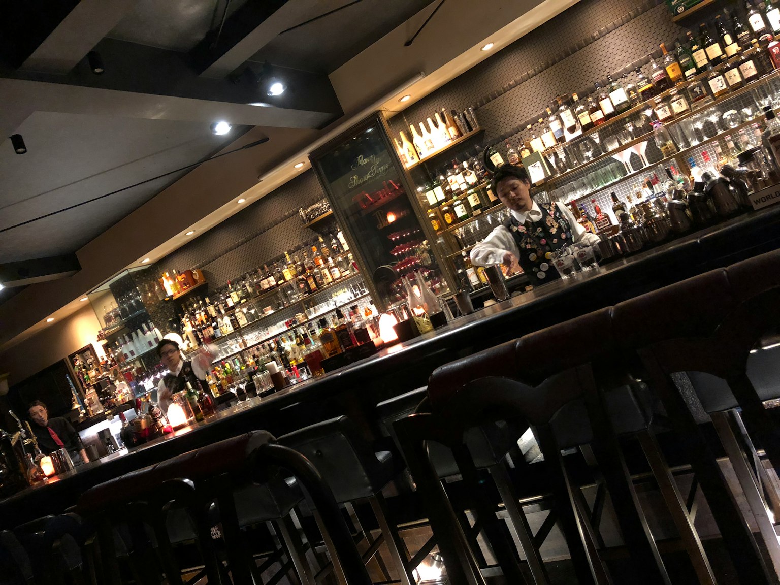 Intérieur d'un bar avec un barman préparant des cocktails et des étagères remplies de bouteilles