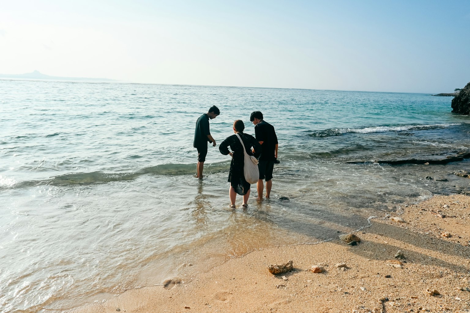 Three people standing at the water's edge playing at the beach
