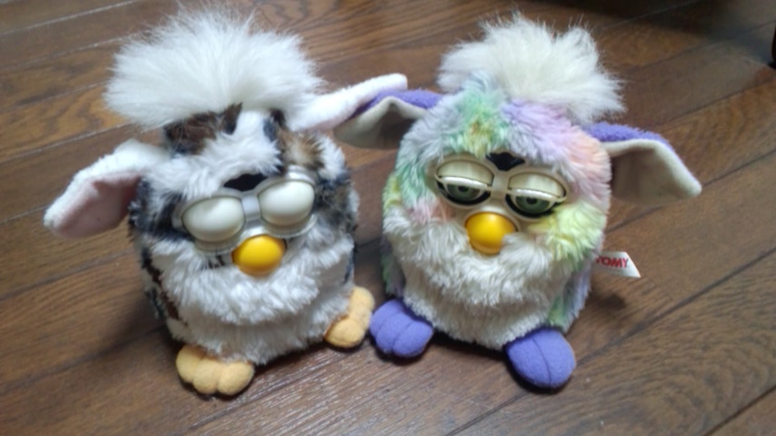 Due Furbies soffici seduti uno accanto all'altro su un pavimento in legno