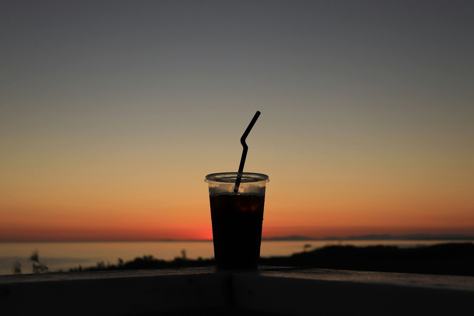 Silhouette of a drink cup with a straw against a sunset