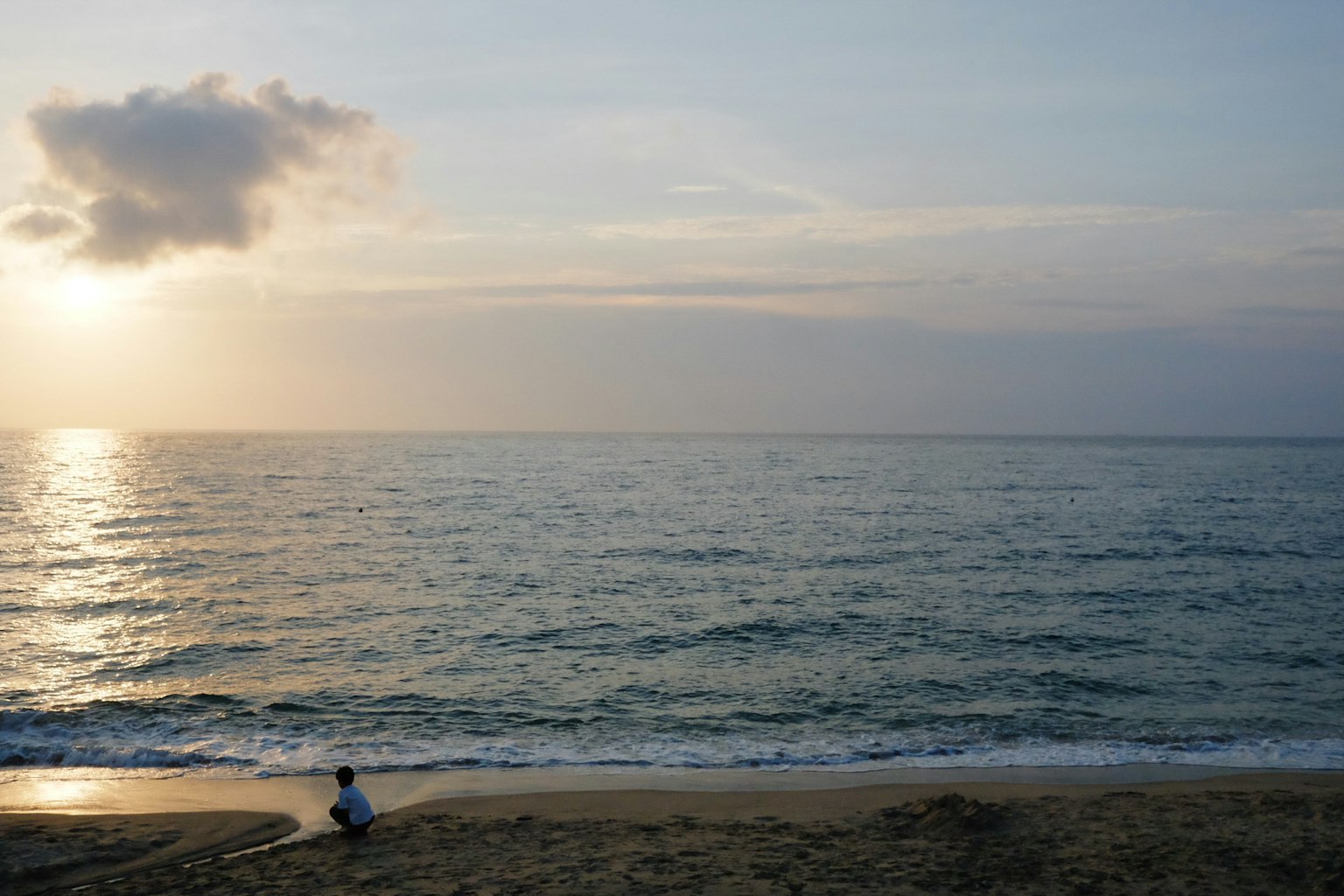 Una persona seduta sulla spiaggia con un mare e un cielo calmi