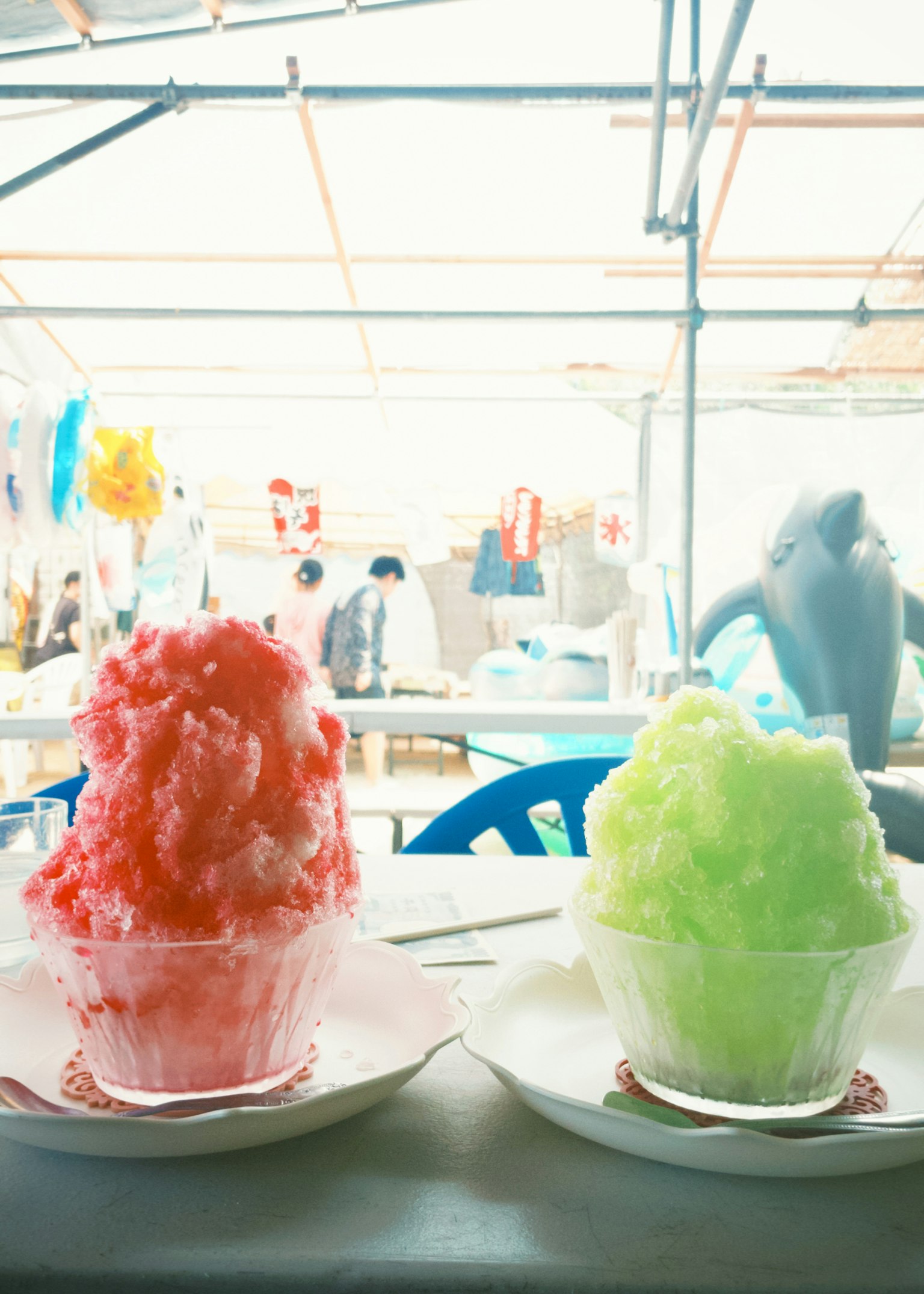 Two shaved ice desserts in clear cups, one red and one green