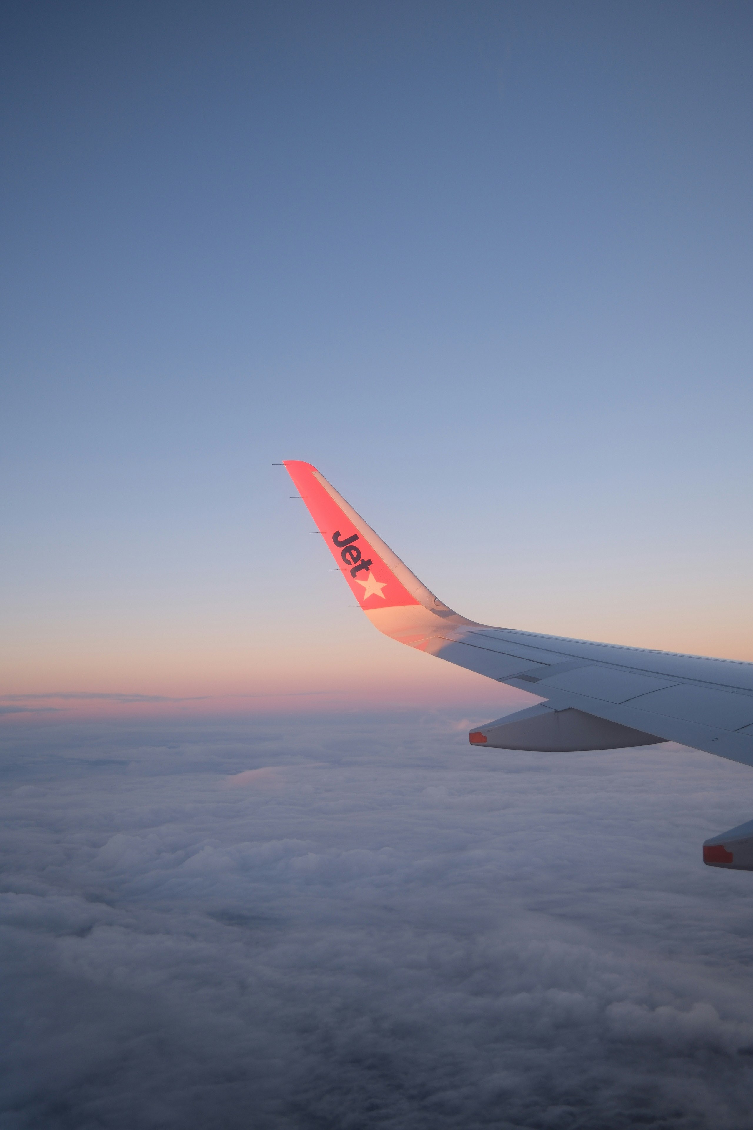 雲の上を飛ぶ飛行機の翼と朝焼けの空