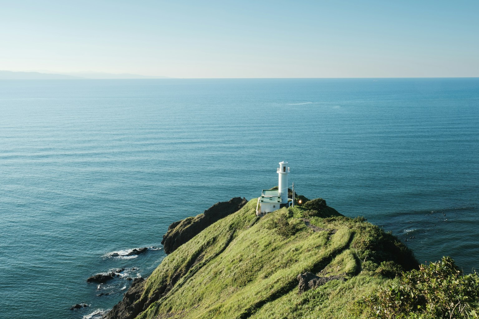 Ein weißer Leuchtturm auf einem grünen Hügel umgeben vom Ozean