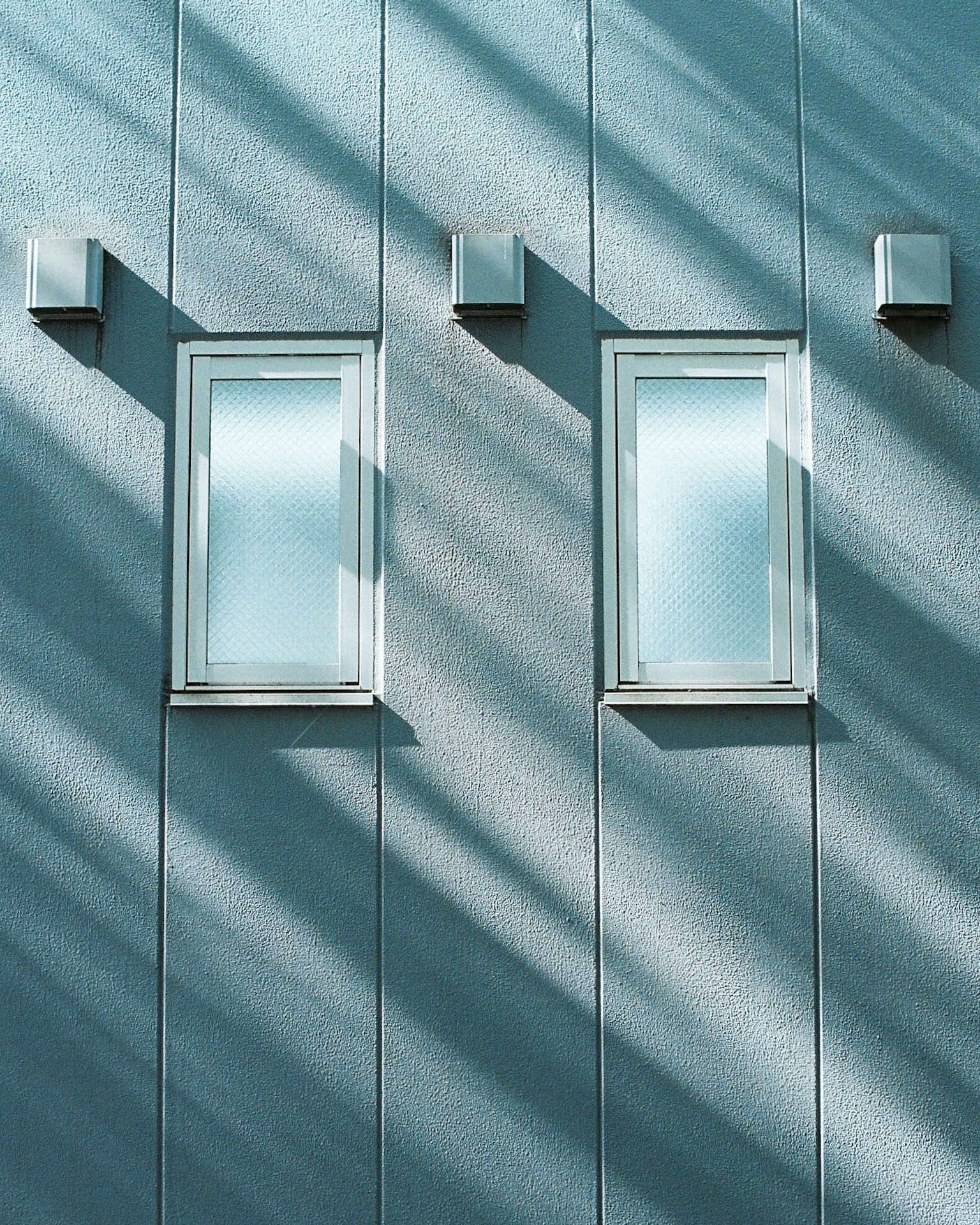 Two windows on a blue wall with diagonal shadows