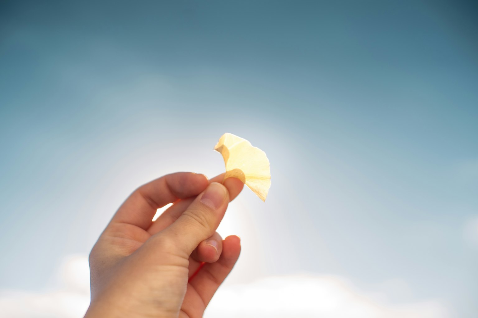 Una mano che tiene uno snack giallo chiaro contro un cielo blu