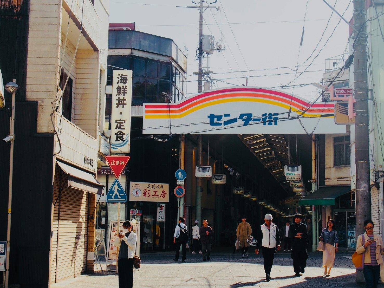 アーケード商店街の入口に並ぶ看板と人々