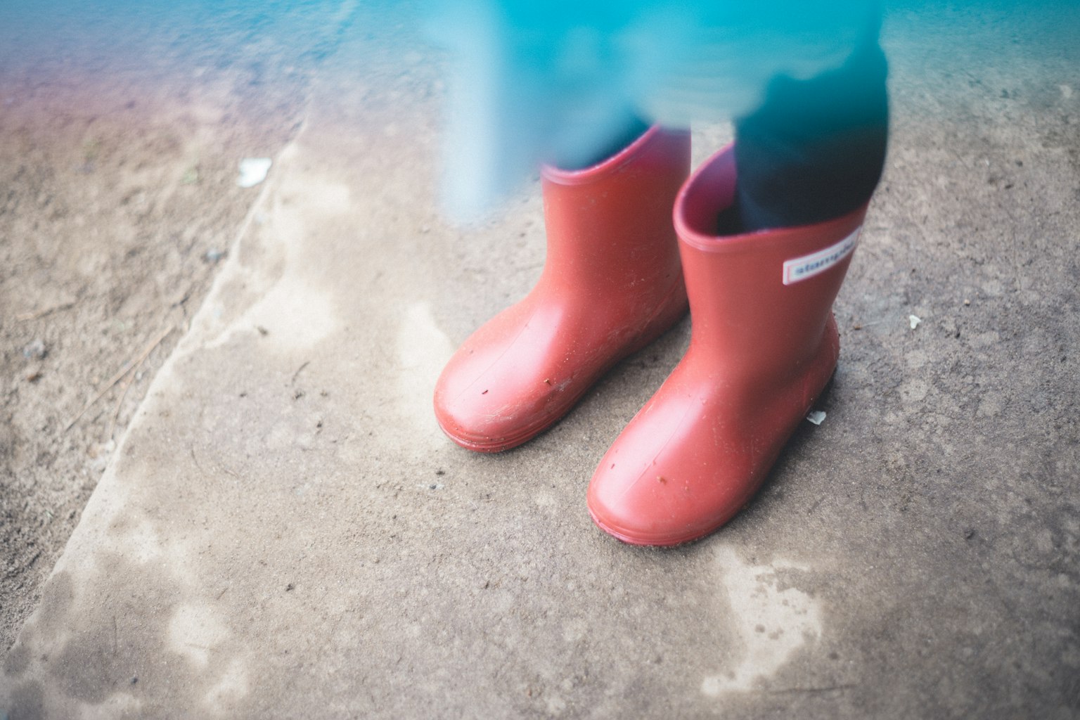 Child's feet in red rubber boots standing on a concrete surface