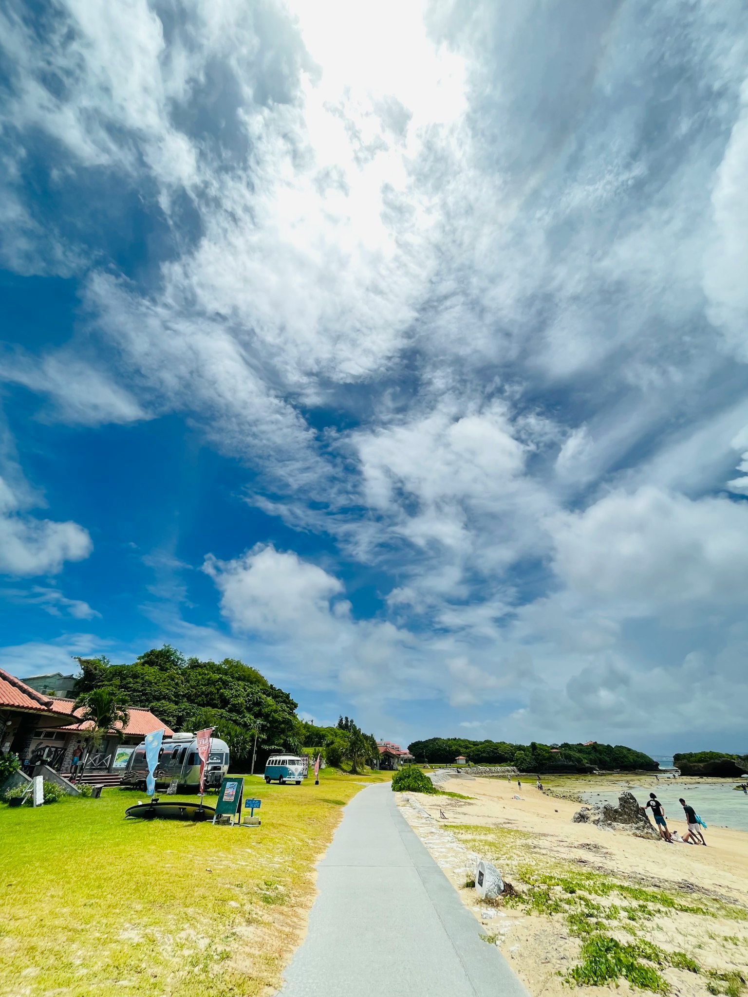 蓝天和白云的海滩风景 绿色草坪和铺成的道路 在海岸上玩耍的人们