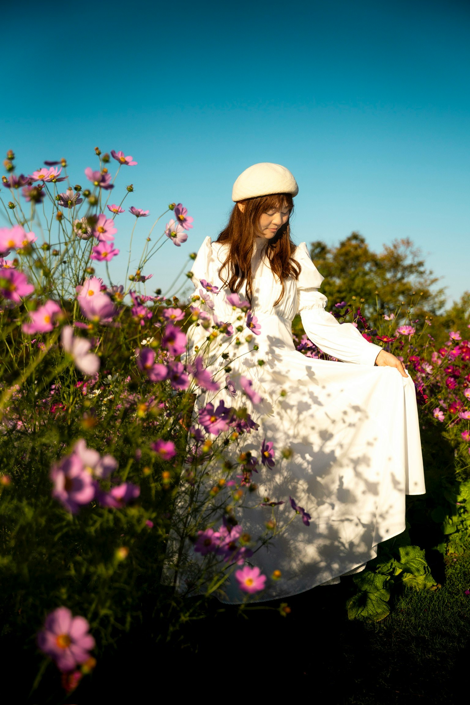 白いドレスを着た女性が色とりどりの花の中に立っている青空の下の風景
