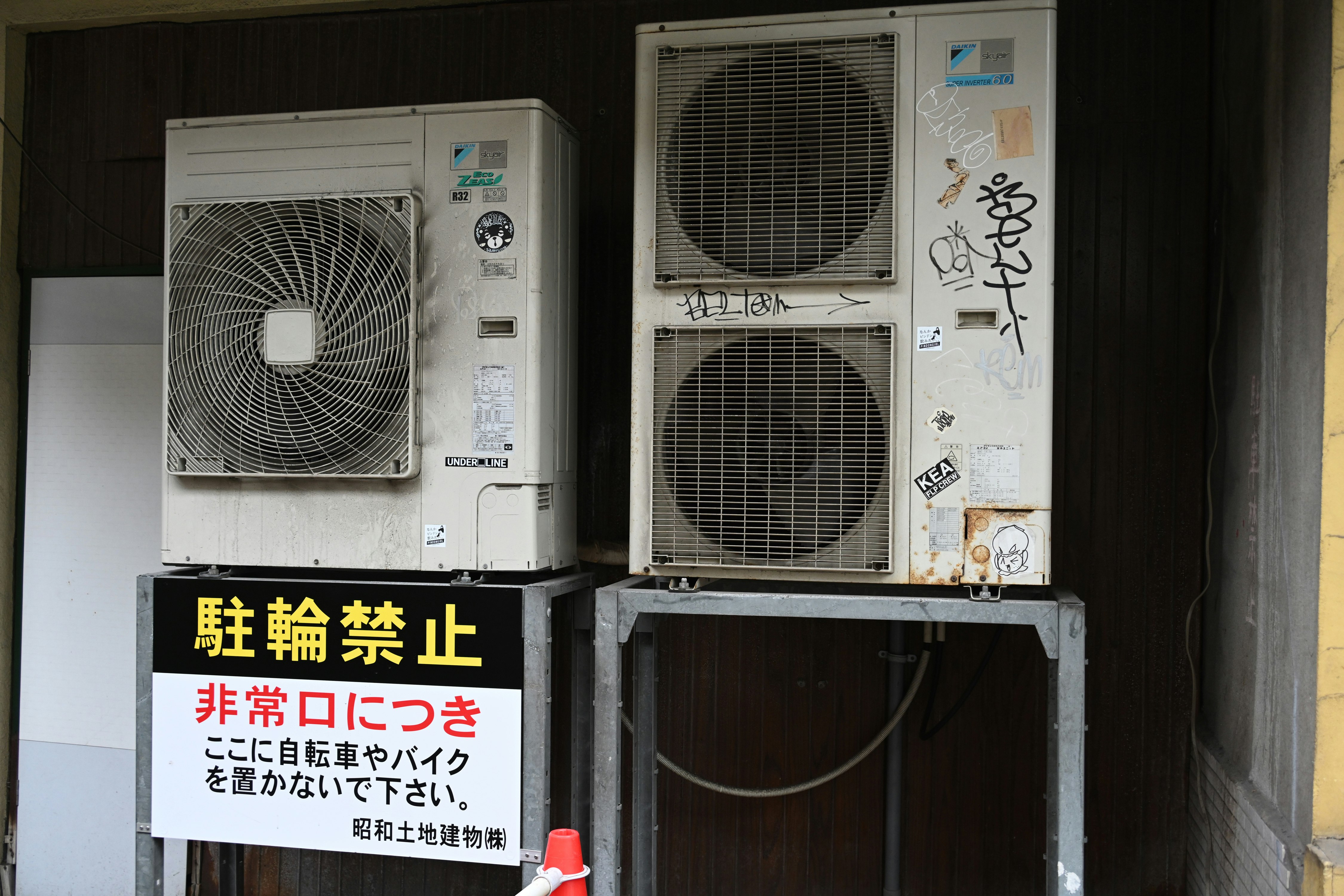 壁際に並ぶ屋外エアコンと注意書きの看板
