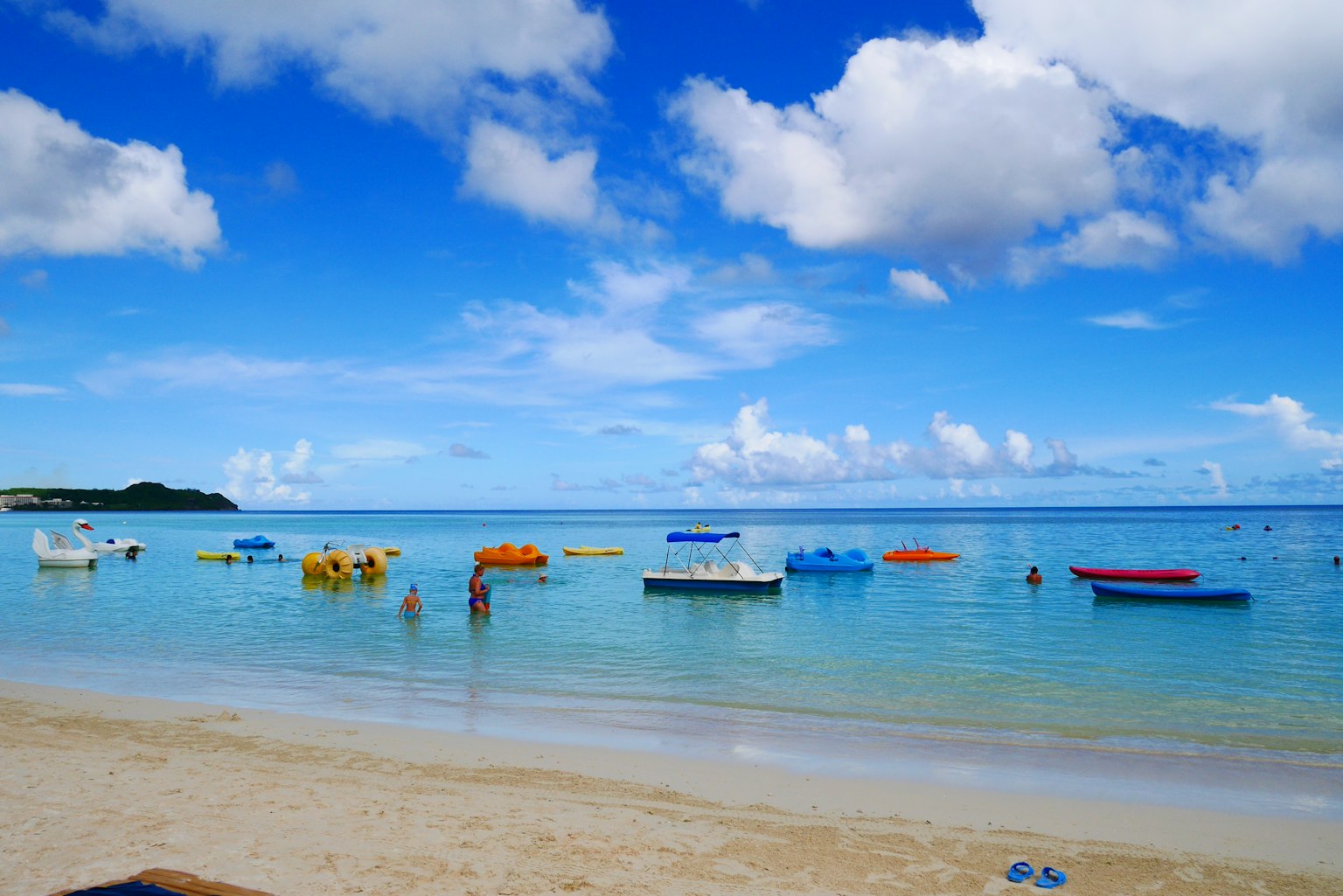 Bateaux colorés flottant sur une plage sereine avec un ciel bleu et des nuages blancs