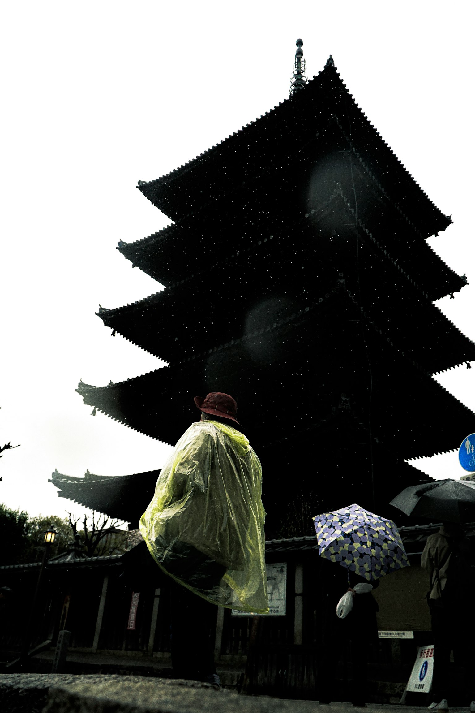 A person walking in the rain with an umbrella in front of a five-story pagoda