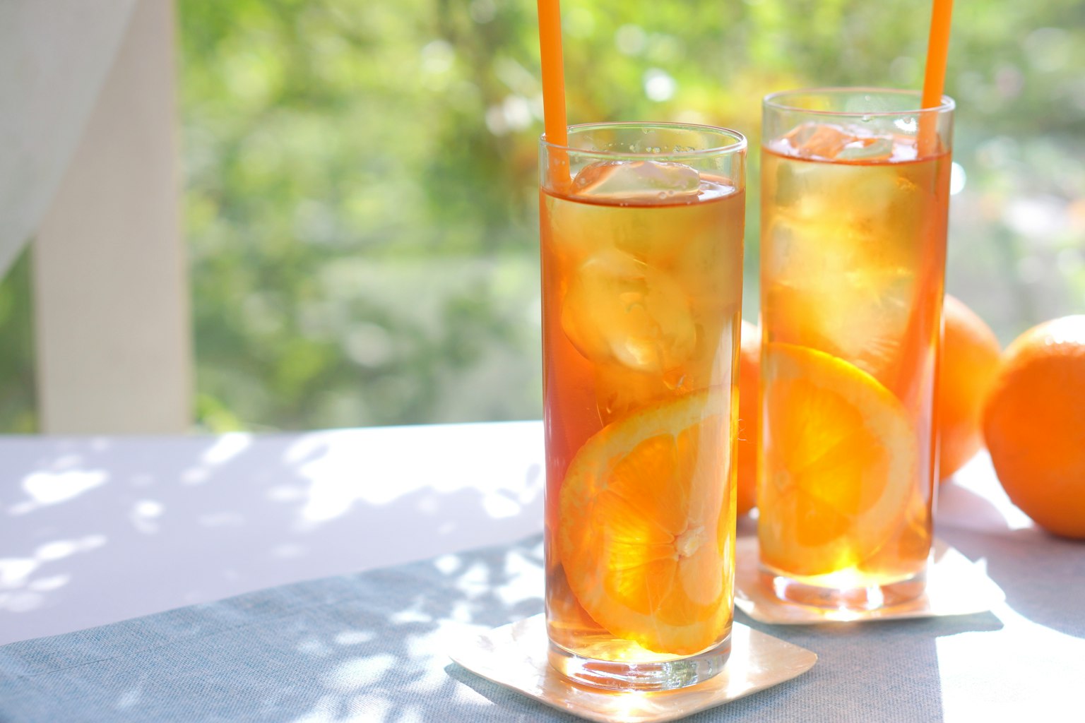 Due alti bicchieri di tè freddo con fette d'arancia su un tavolo soleggiato