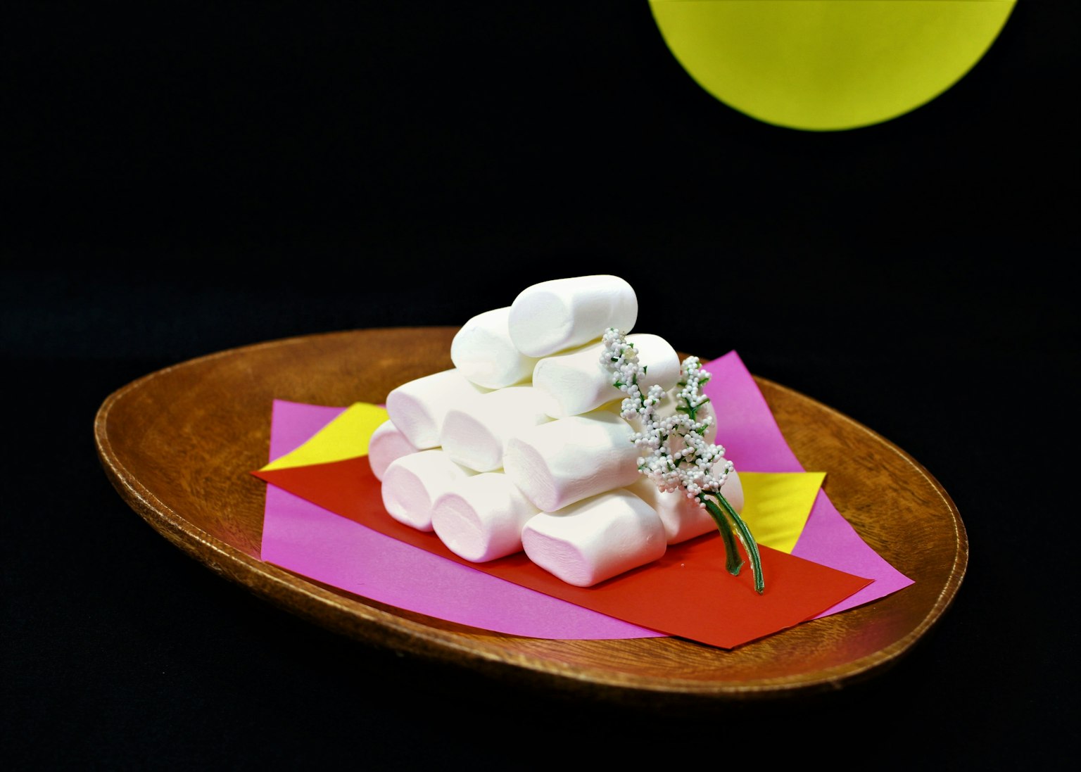 A stack of white marshmallows on a colorful paper background with a flower garnish