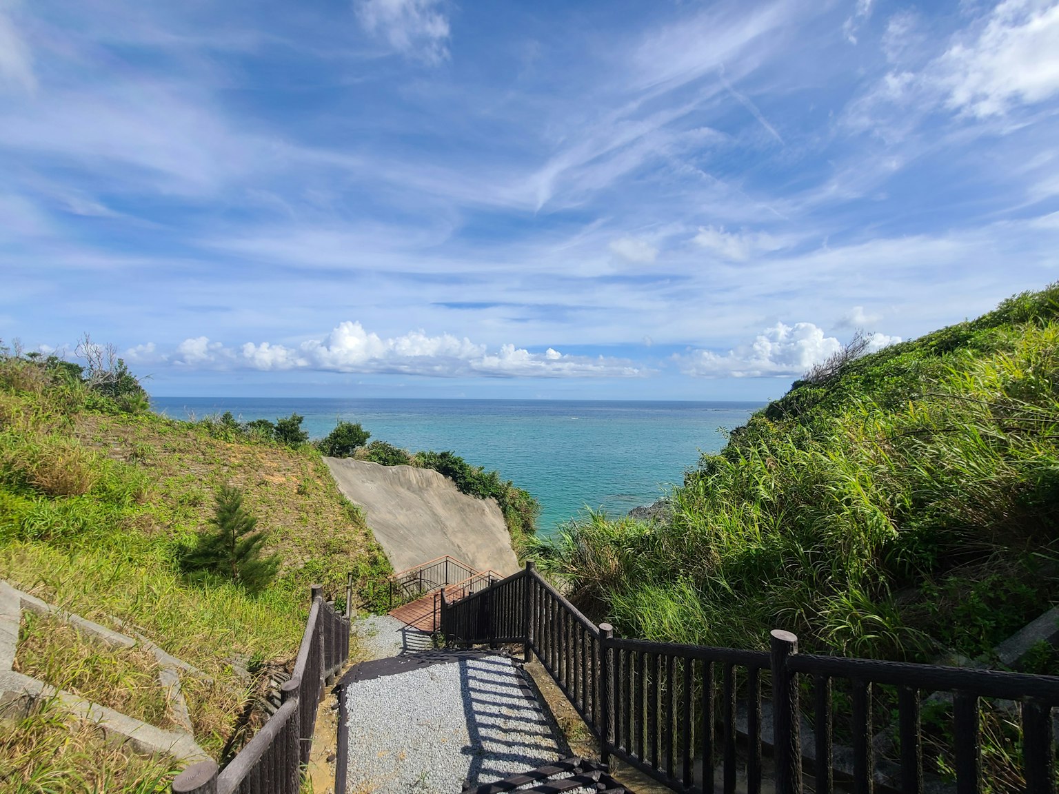 Pemandangan indah laut biru dan langit dengan bukit hijau dan tangga kayu