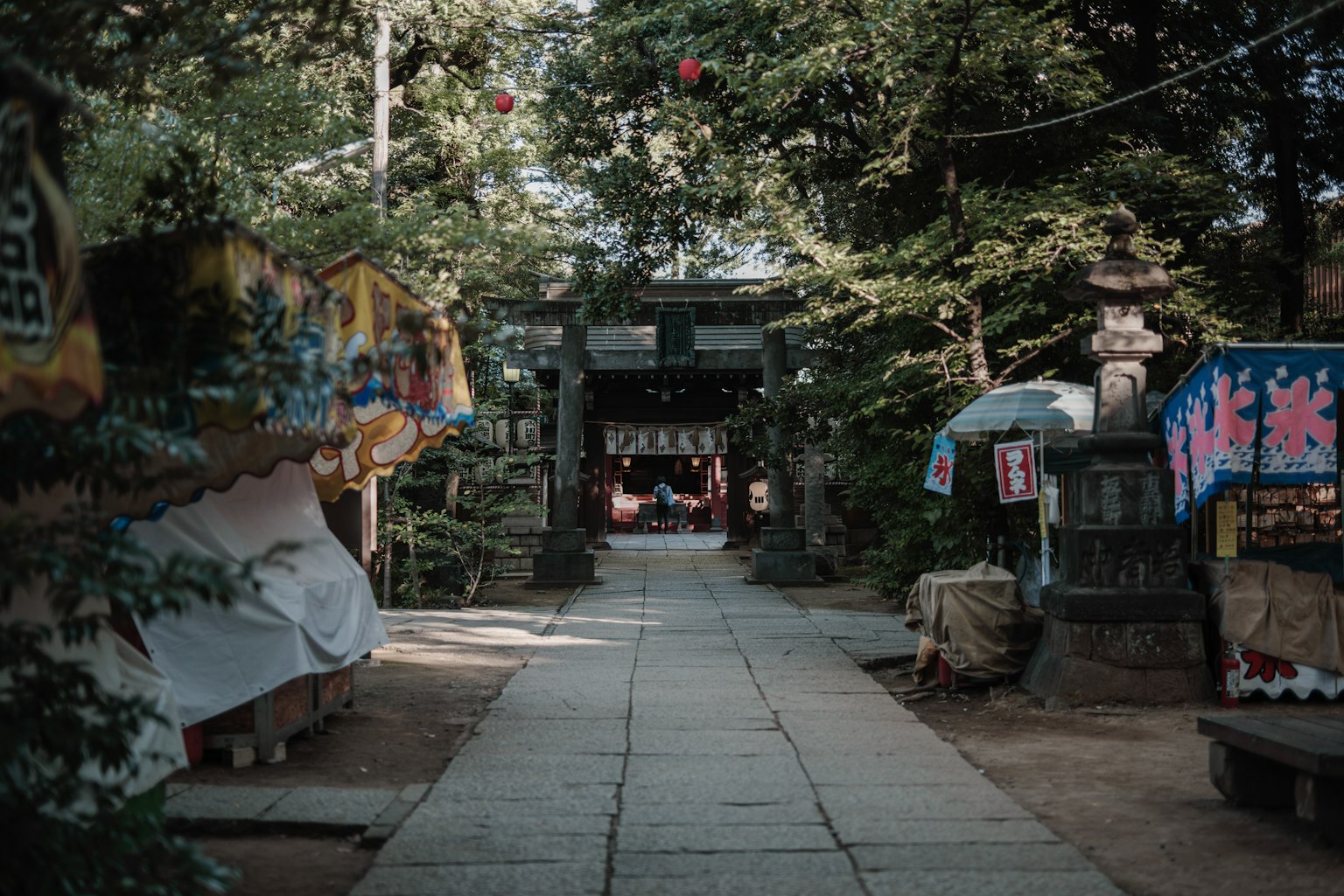Quiet shrine pathway lined with colorful stalls and green trees